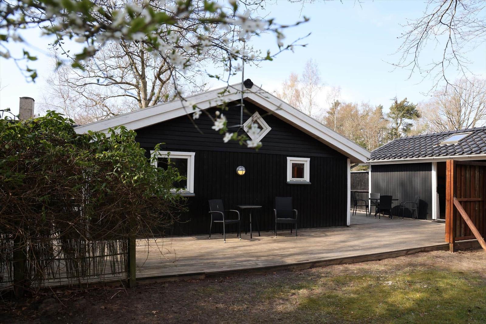 Black house with wooden terrace and garden. Outdoor area with seating and trees.