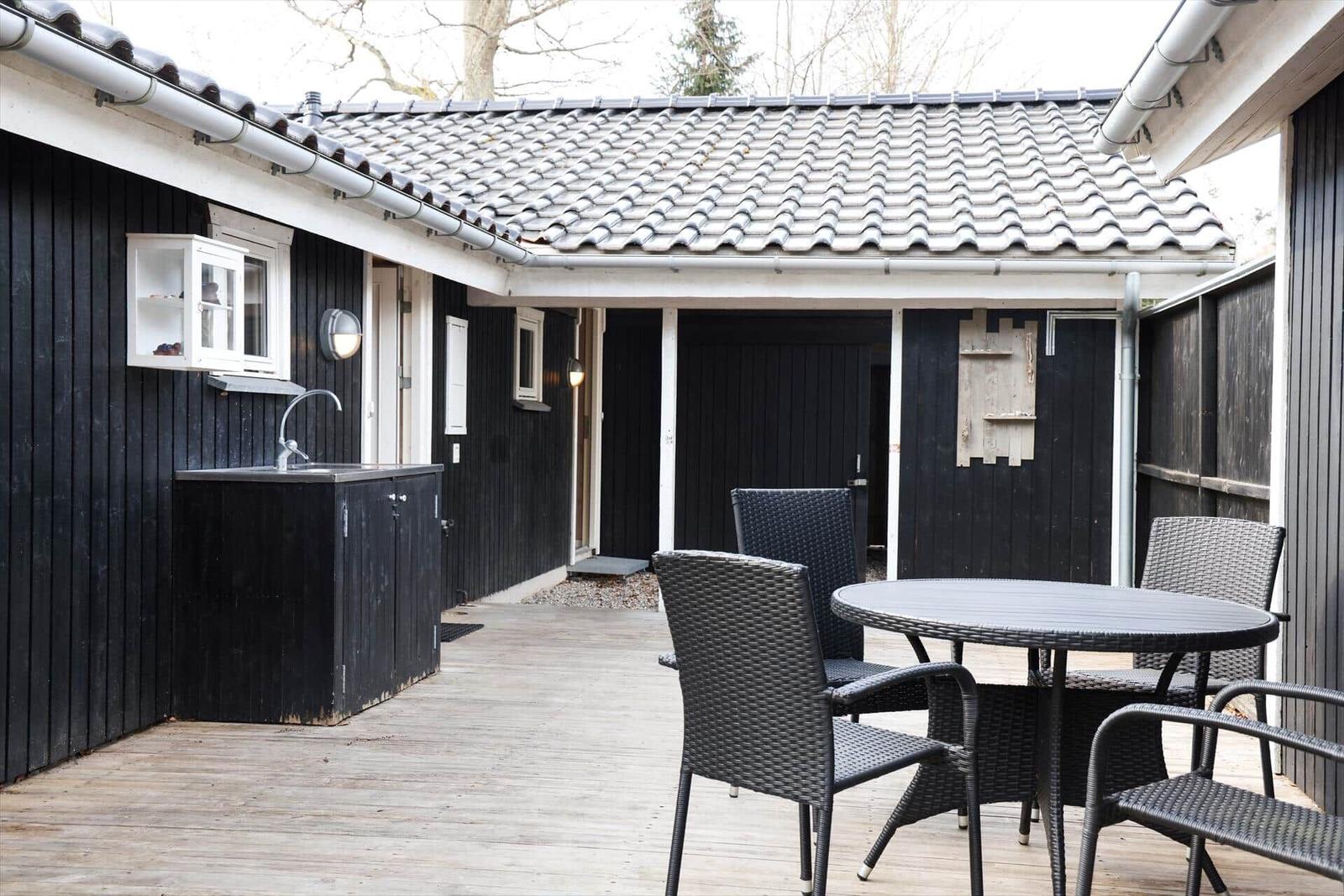 Terrace with table, chairs, and outdoor kitchen at black wooden house.