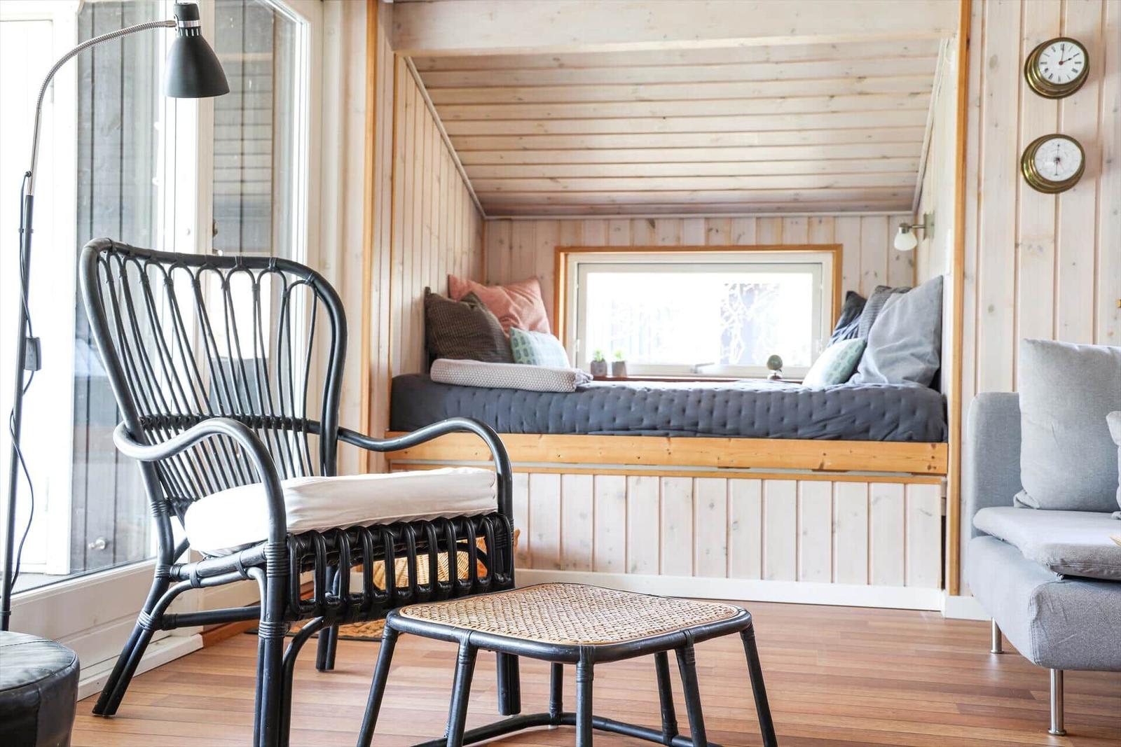 A room with wooden walls, bed under window, chair and stool.