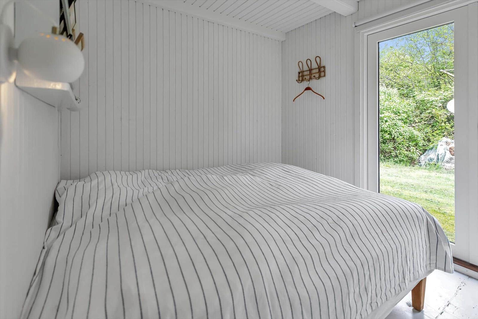 Schlafzimmer mit Bett, weißen Wänden und Blick auf Garten.