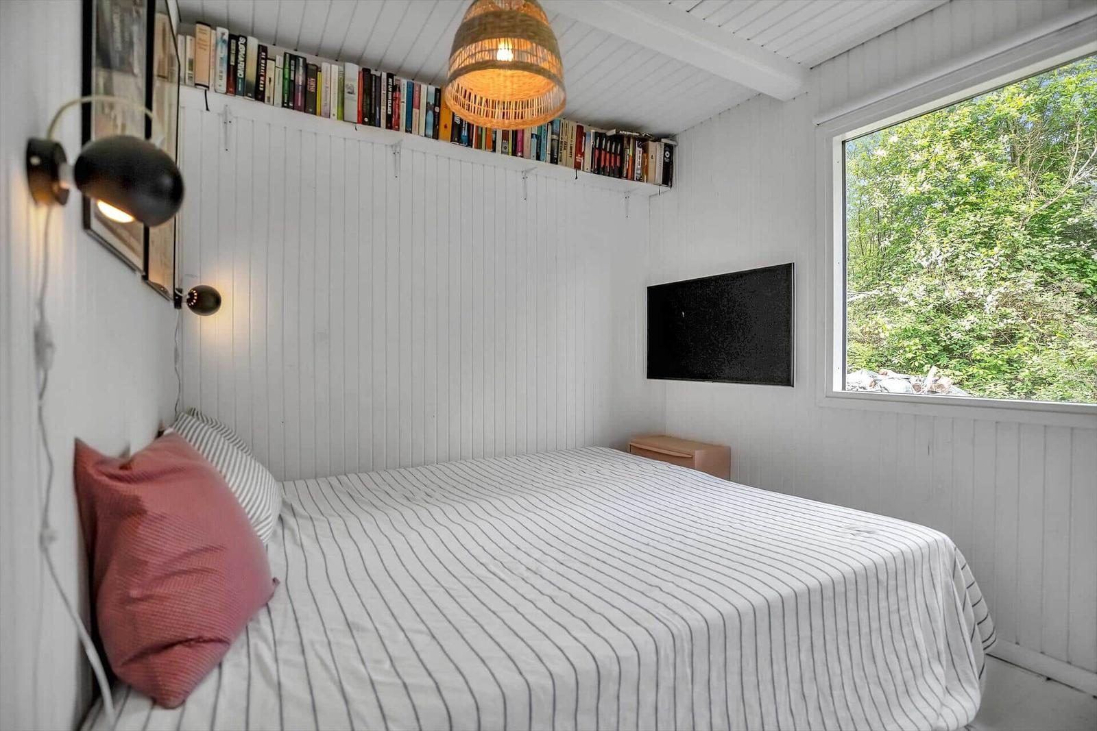 Schlafzimmer mit Bett, Fernseher und Bücherregal an der Wand.