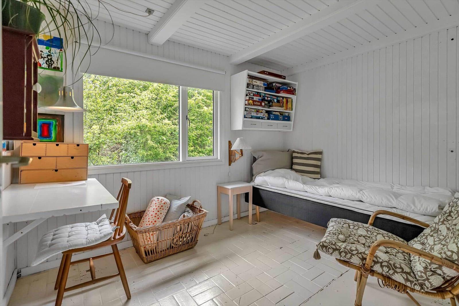 Zimmer mit Bett, Schreibtisch, Stuhl und Fenster mit Blick auf Bäume.