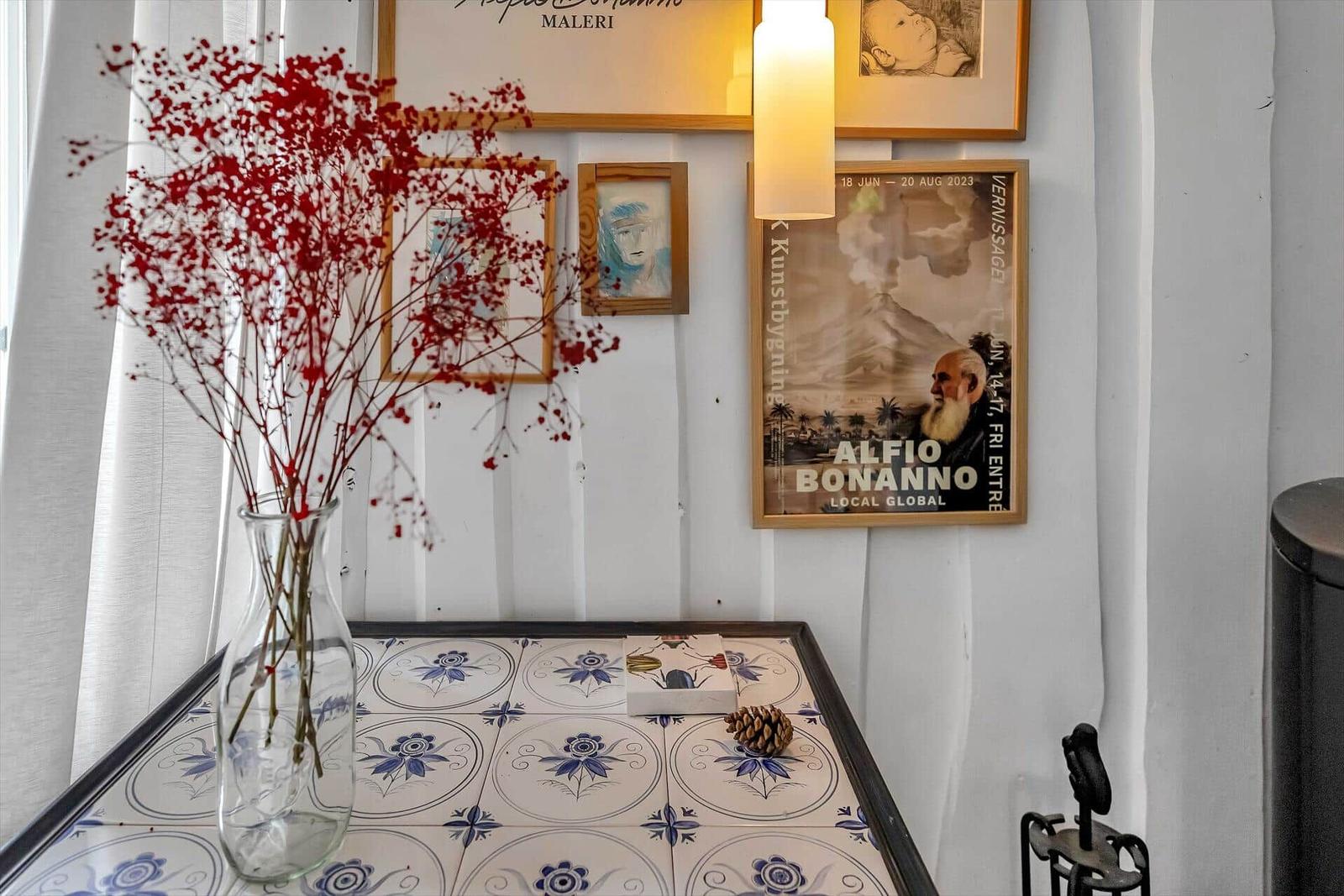 Tisch mit blau-weißen Fliesen, Vase mit roten Zweigen und Wanddekoration.