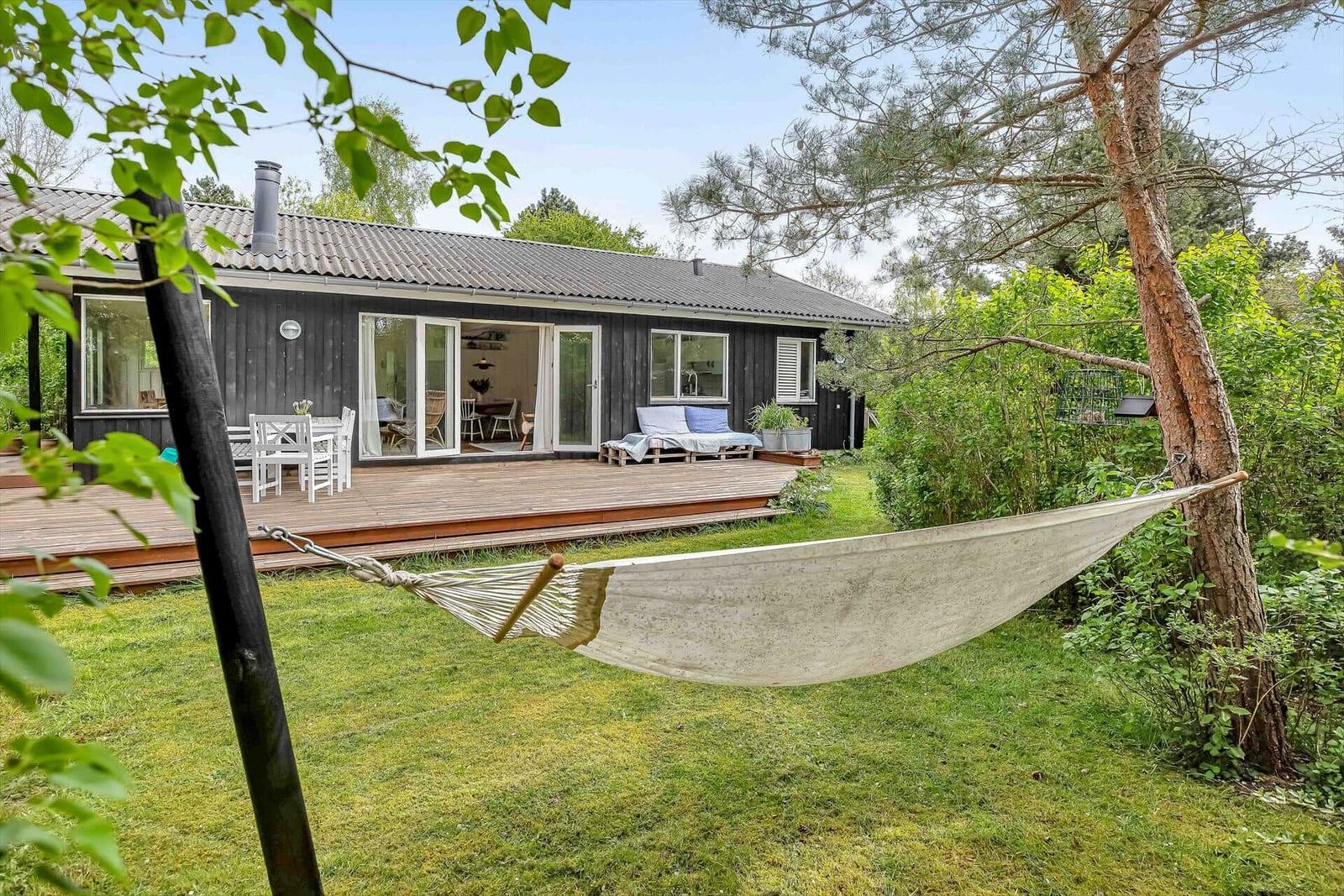 Hängemattenschaukel im Garten neben einer Holzhütte mit Terrasse und Gartenmöbeln.