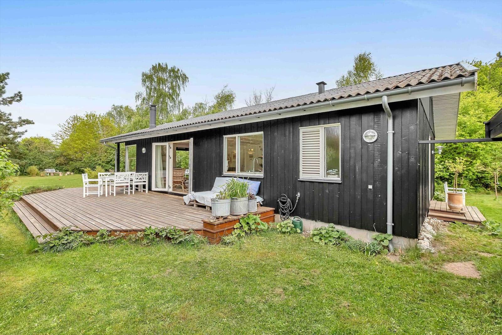 Schwarze Holzhütte mit Terrasse und Garten. Weiße Möbel und Pflanzen.