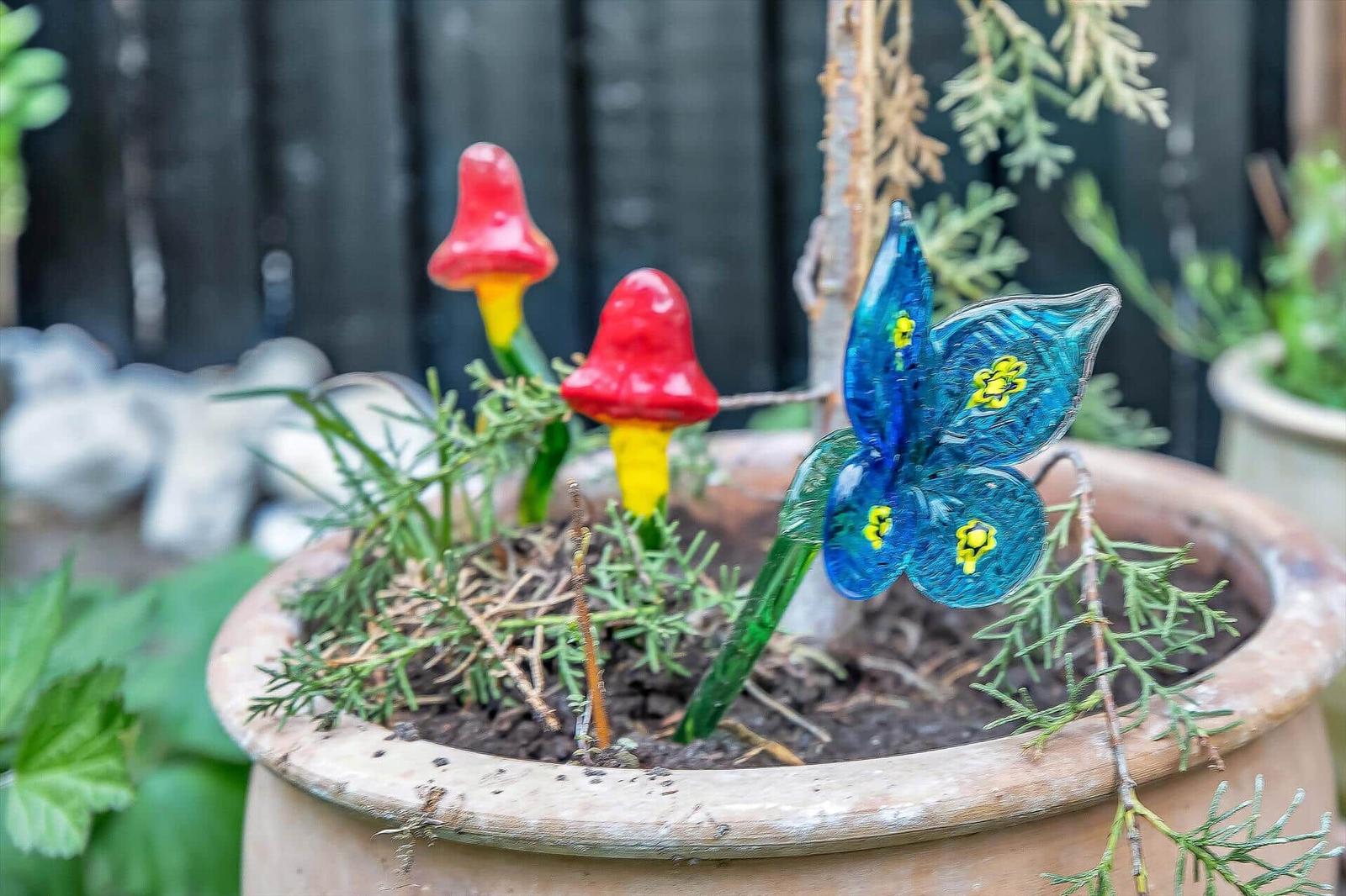 Terrassenkübel mit Glasfiguren: zwei Pilze und ein Schmetterling.