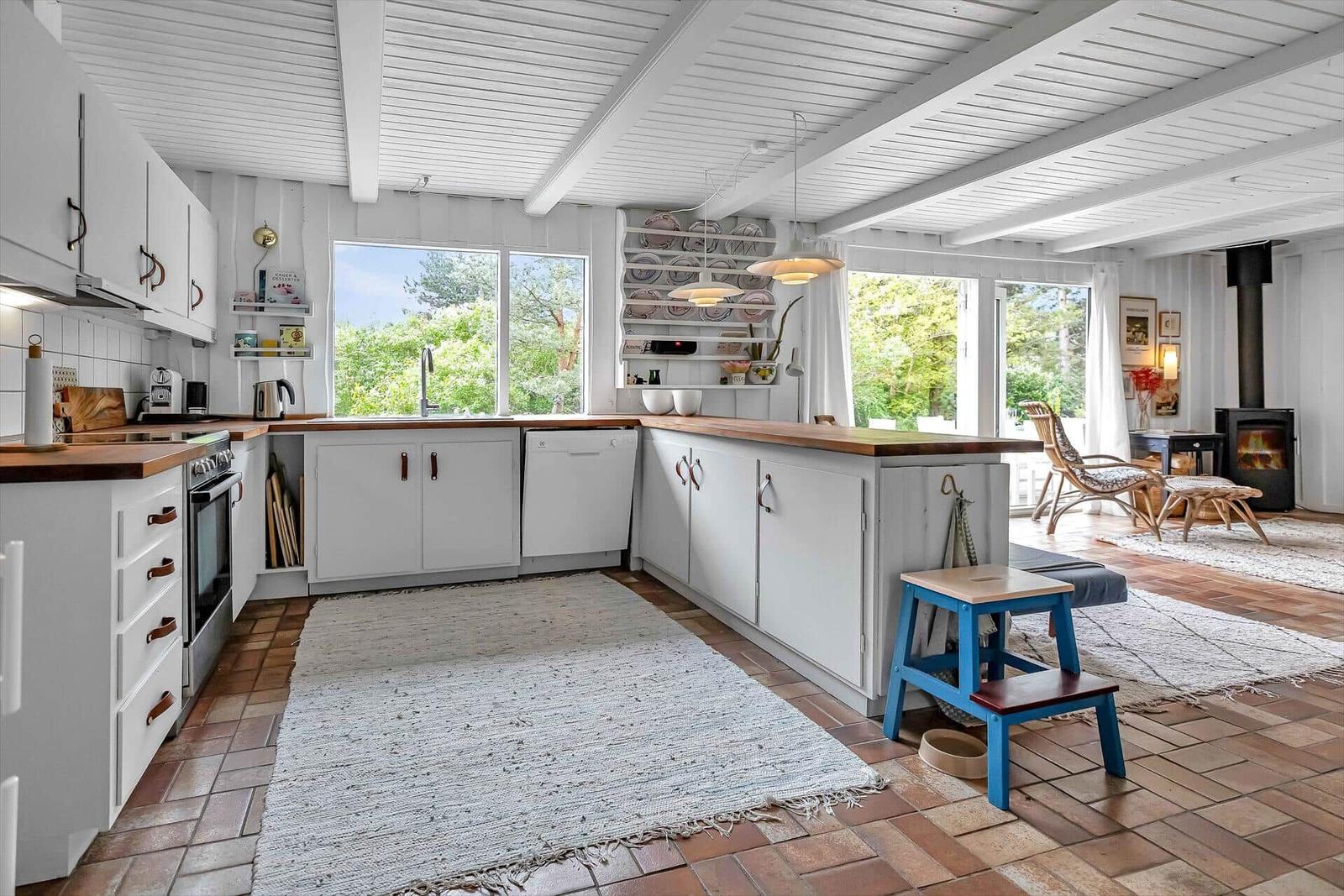 Küche mit Holzoberflächen und Blick auf Garten. Wohnbereich mit Kamin und Sitzgelegenheit.