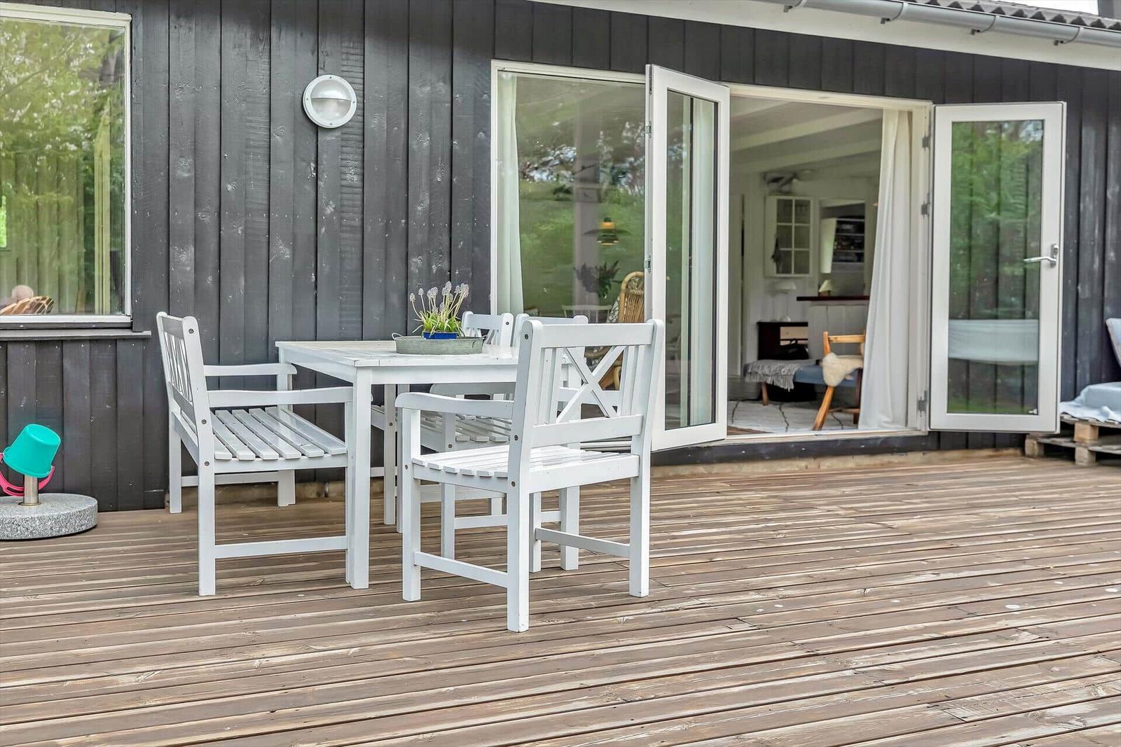 Terrasse mit weißem Tisch und Stühlen, Schiebetür führt ins Haus.