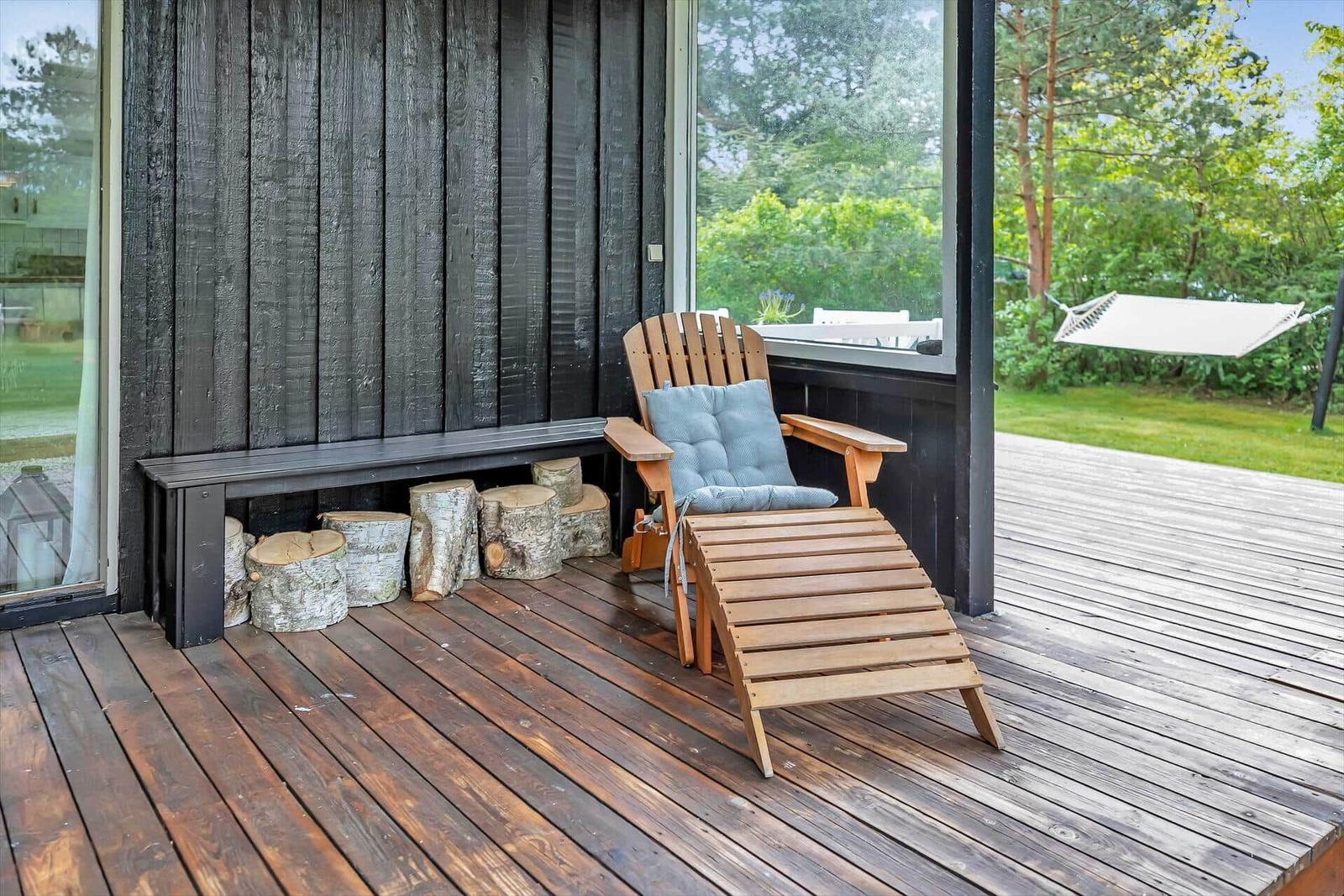 Terrasse mit Holzstuhl, Kissen und Baumstumpfen. Hintergrund: Grünfläche und Hängemattensitz.