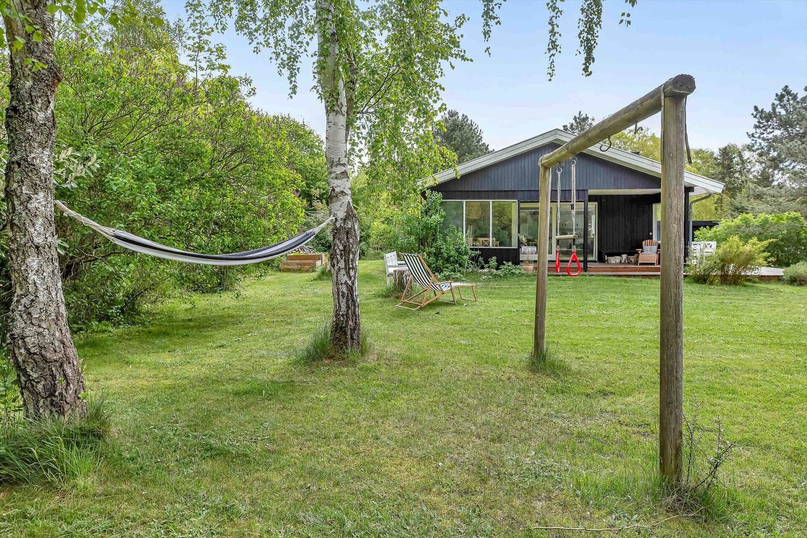 Haus mit Garten, Hängematten und Schaukel. Grünflächen und Bäume umgeben die Terrasse.