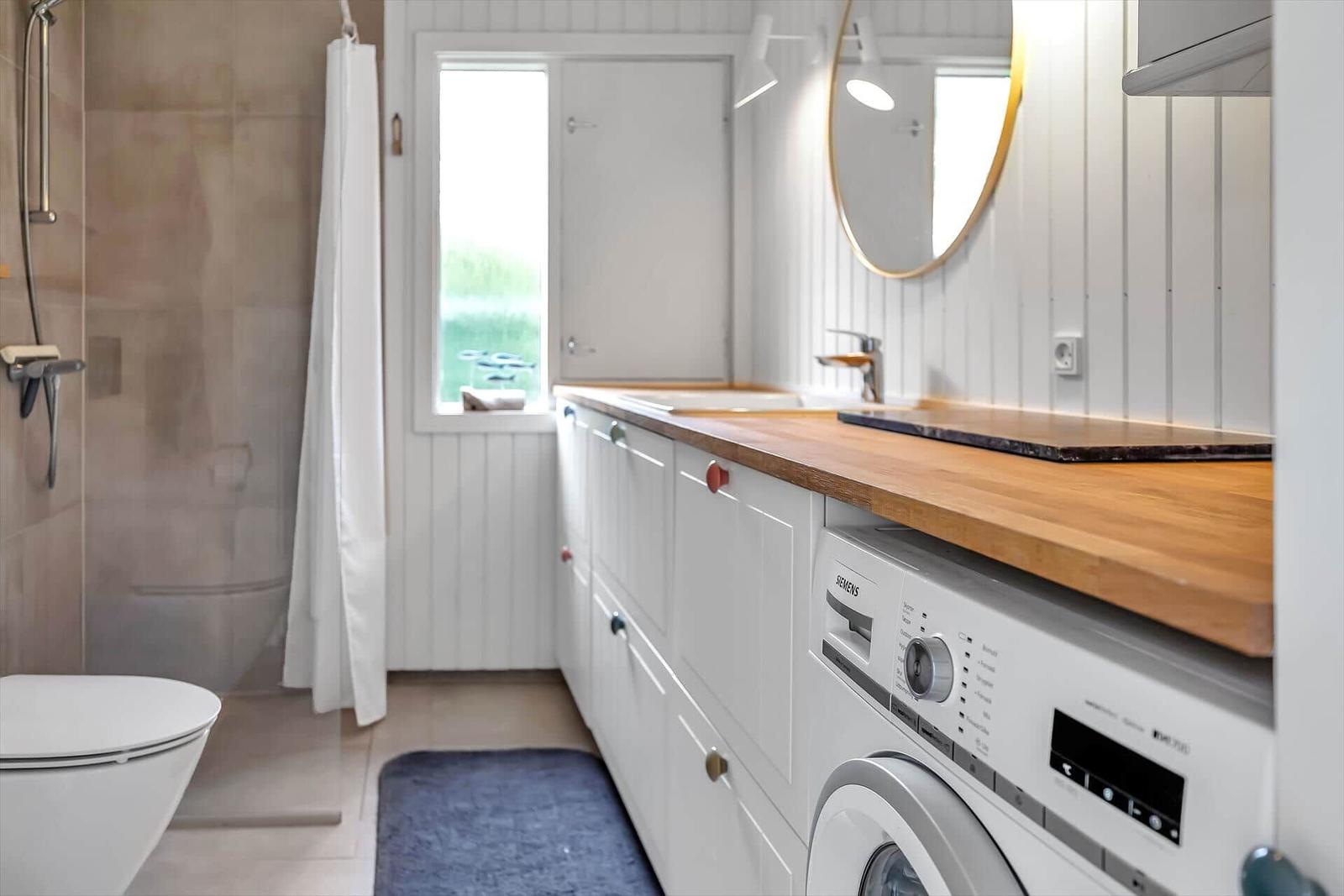 Badezimmer mit Dusche, Waschmaschine und Holz-Arbeitsplatte.