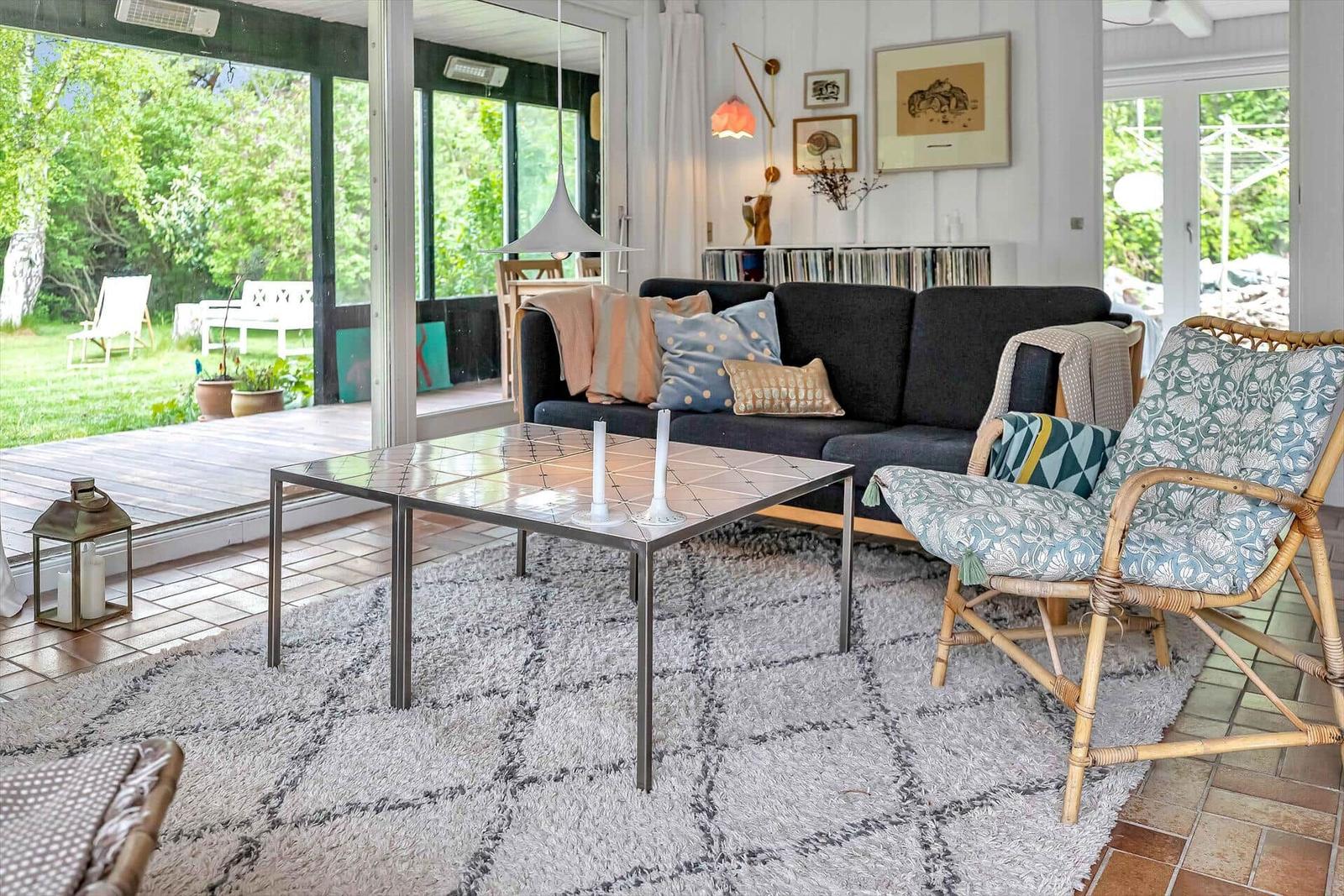 Ein Wohnzimmer mit Sofa, Stuhl und Tisch. Durchgänge führen zu einer Terrasse mit Garten.