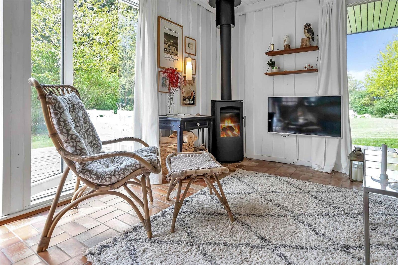 Wohnzimmer mit Stuhl, Kamin und Fernseher. Große Fenster mit Blick auf Garten.
