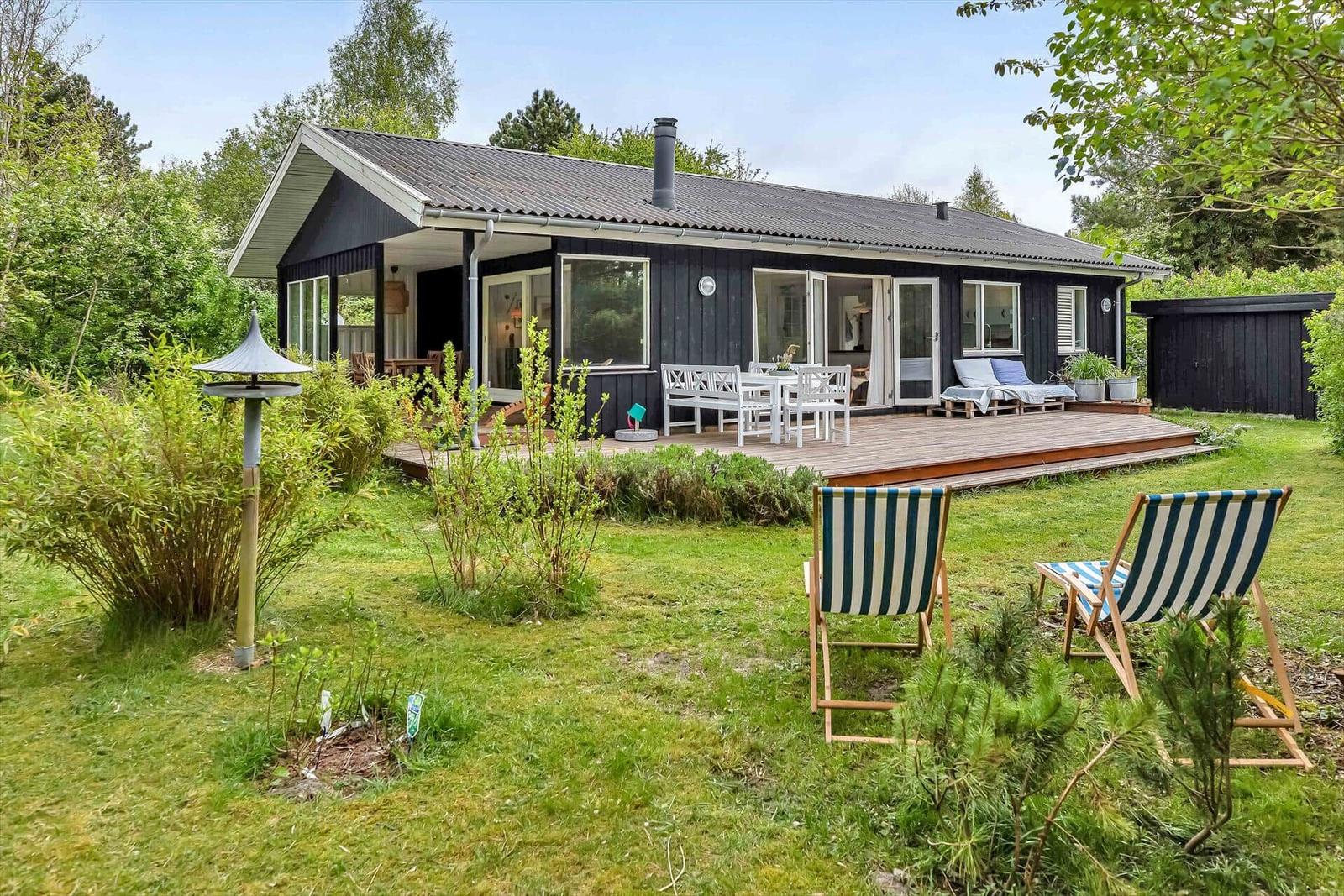 Schwarzes Haus mit Terrasse, Garten und Liegestühlen.