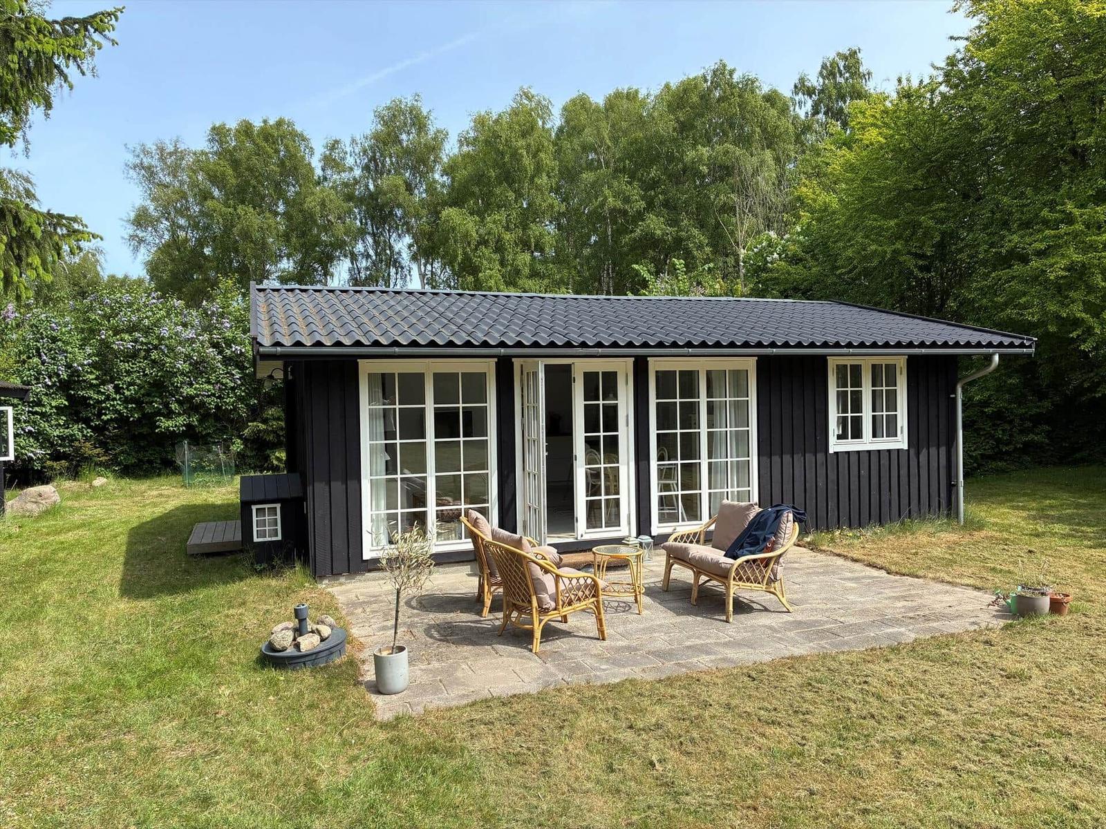 Black wooden house with terrace, garden, and trees in the background.