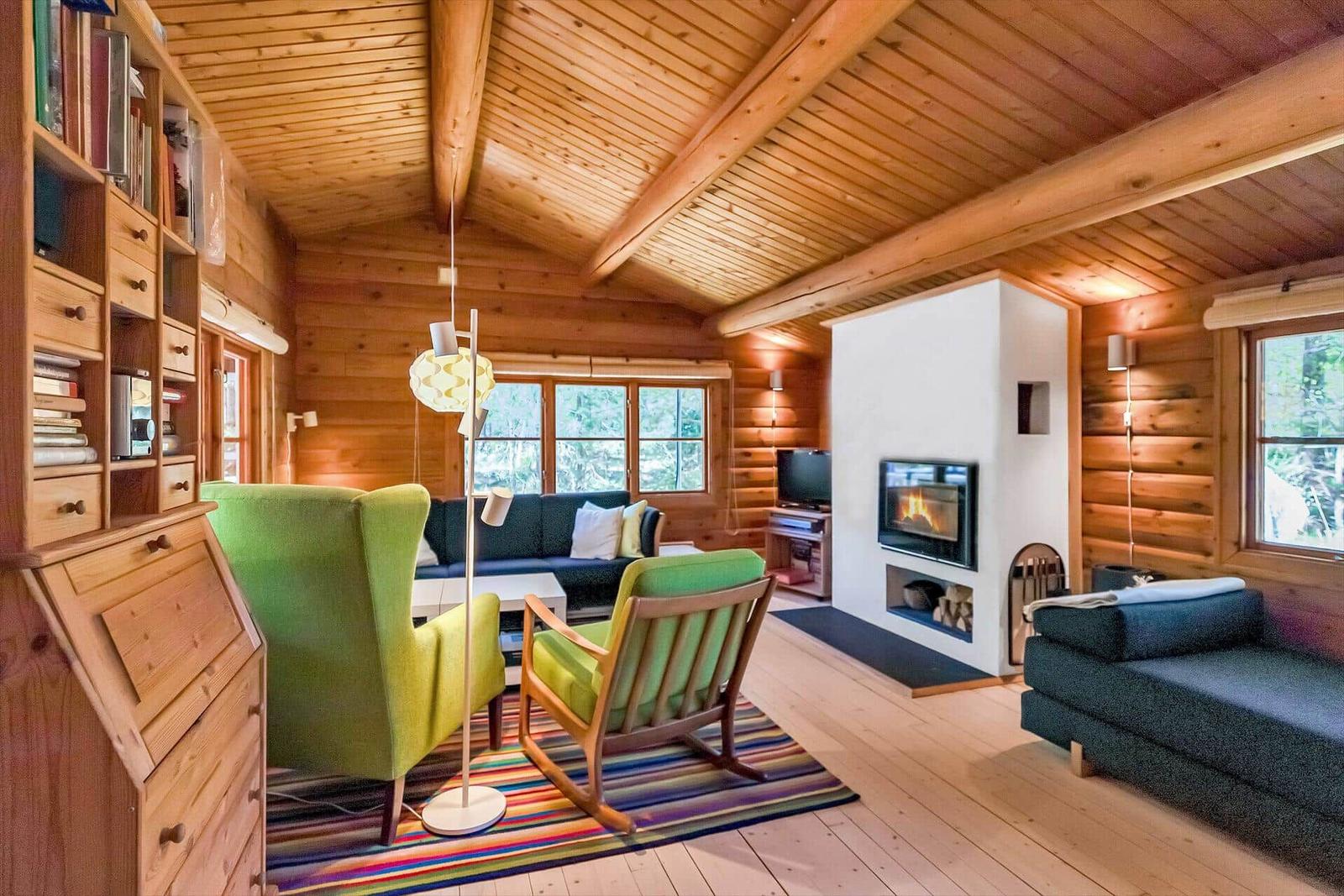 Wohnzimmer mit Holzdecke, Kamin und grünen Sesseln.