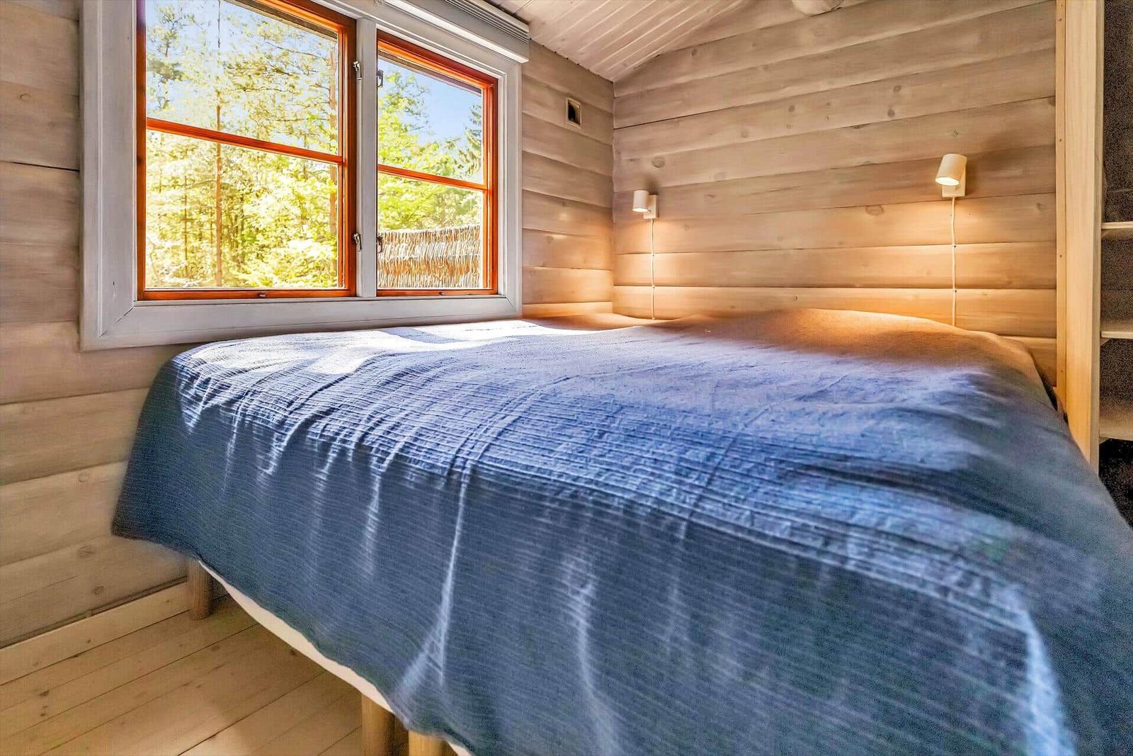 Ein Bett mit blauer Bettwäsche vor einem Fenster mit Waldblick.