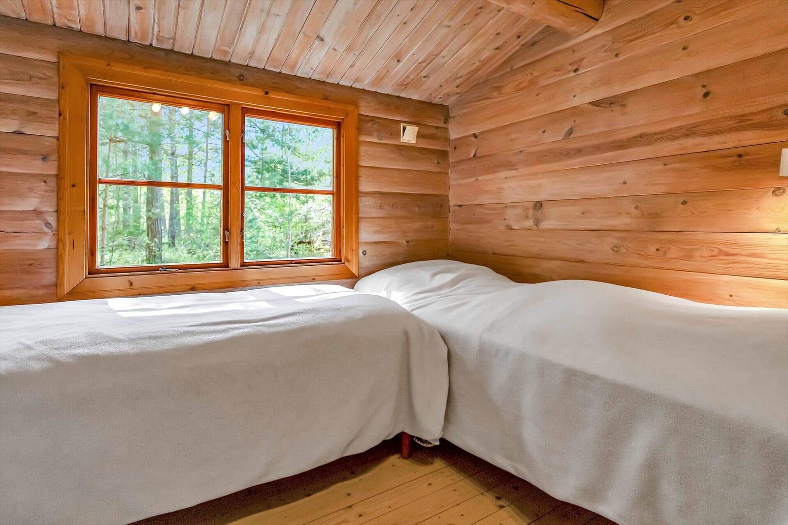 Zwei Betten in einem Holzhauszimmer mit Fensterblick auf Wald.