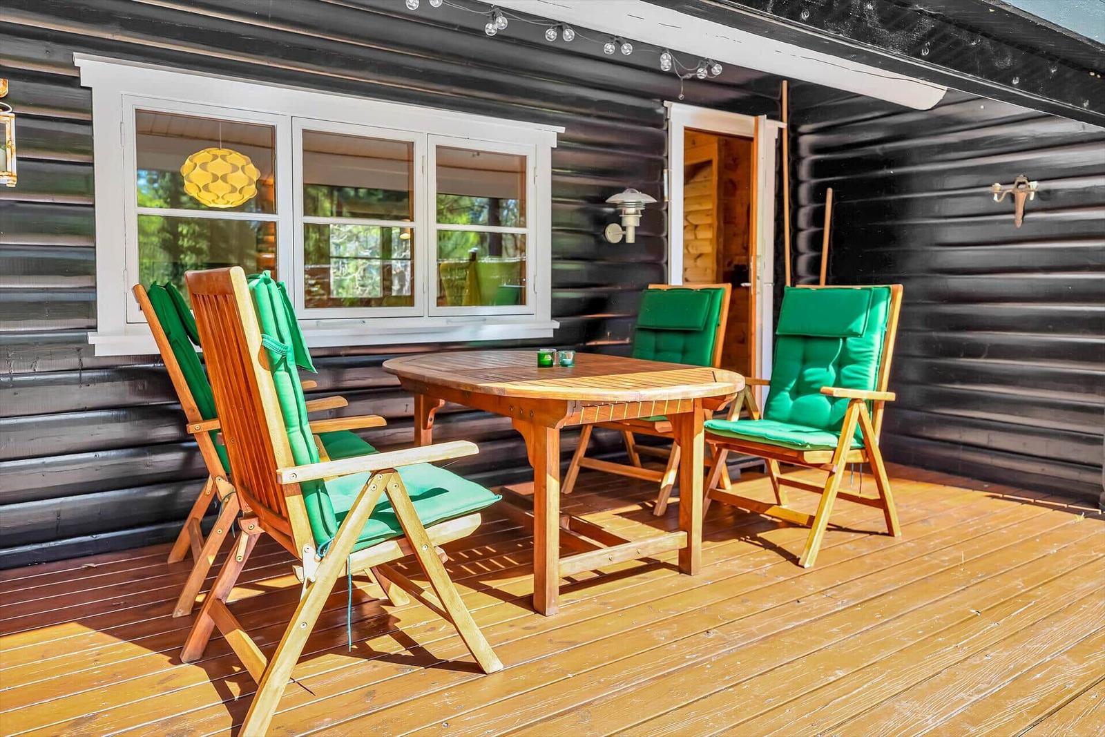 Terrasse mit Holztisch und grünen Stühlen vor einem Holzhaus.