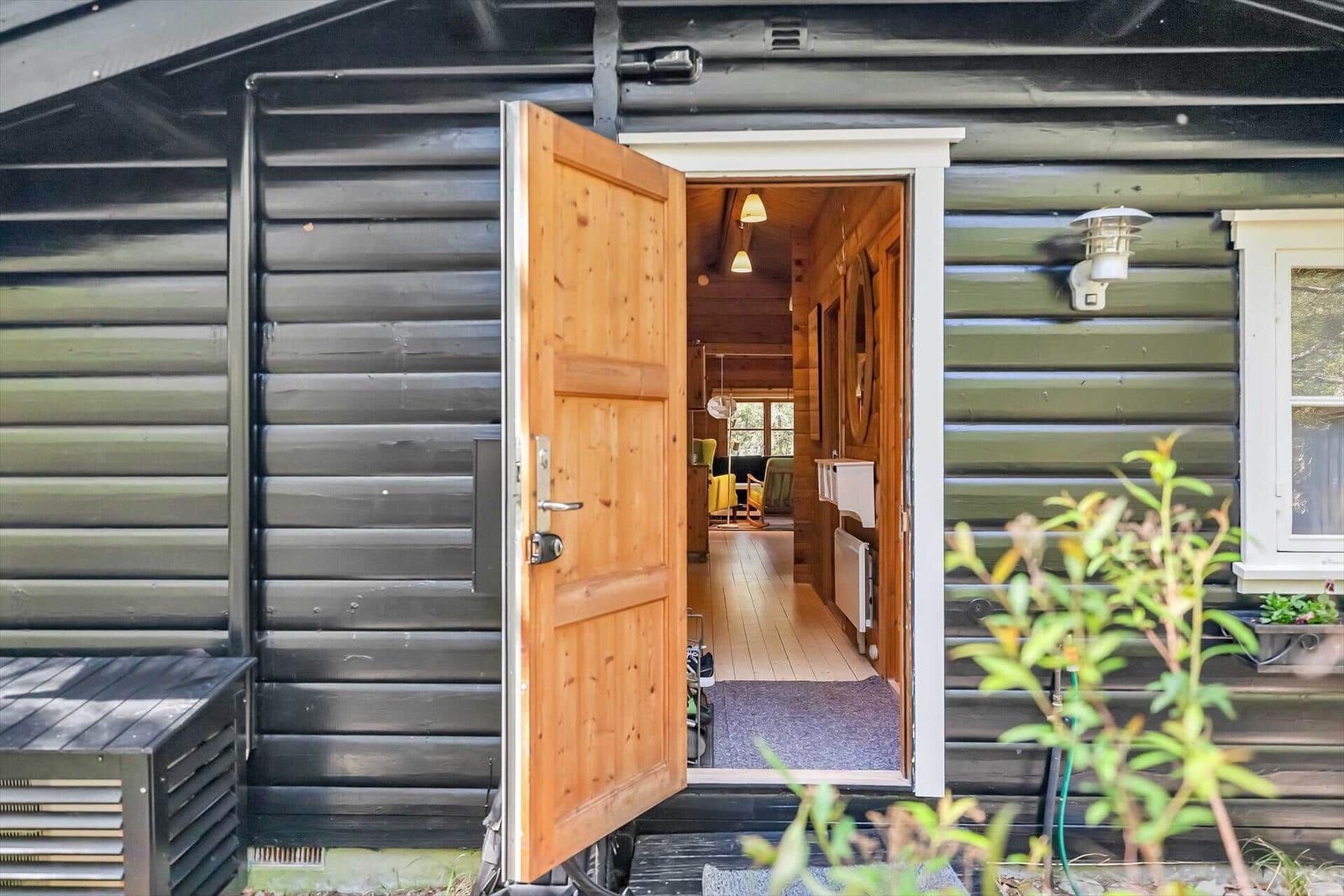 Holztür öffnet den Blick in das Innere des Hauses mit Holzboden und Fenster.