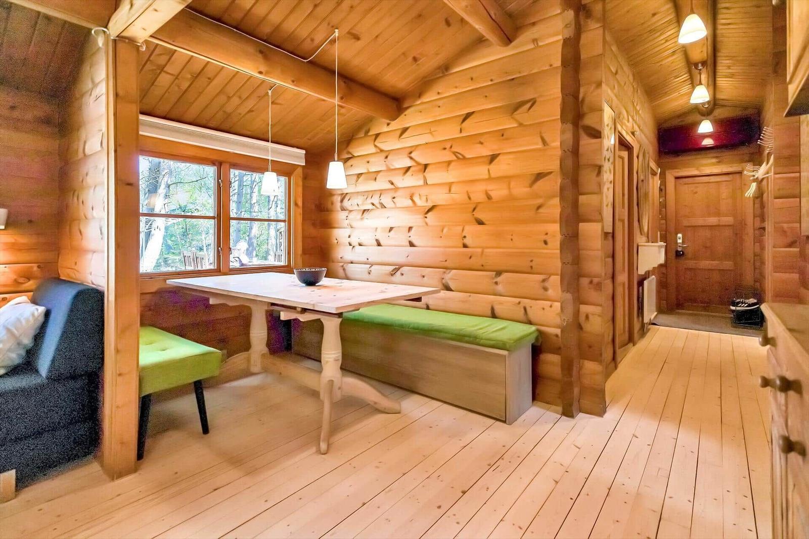 Holzhaus mit Essbereich, grüner Sitzbank und Fenster zum Wald.