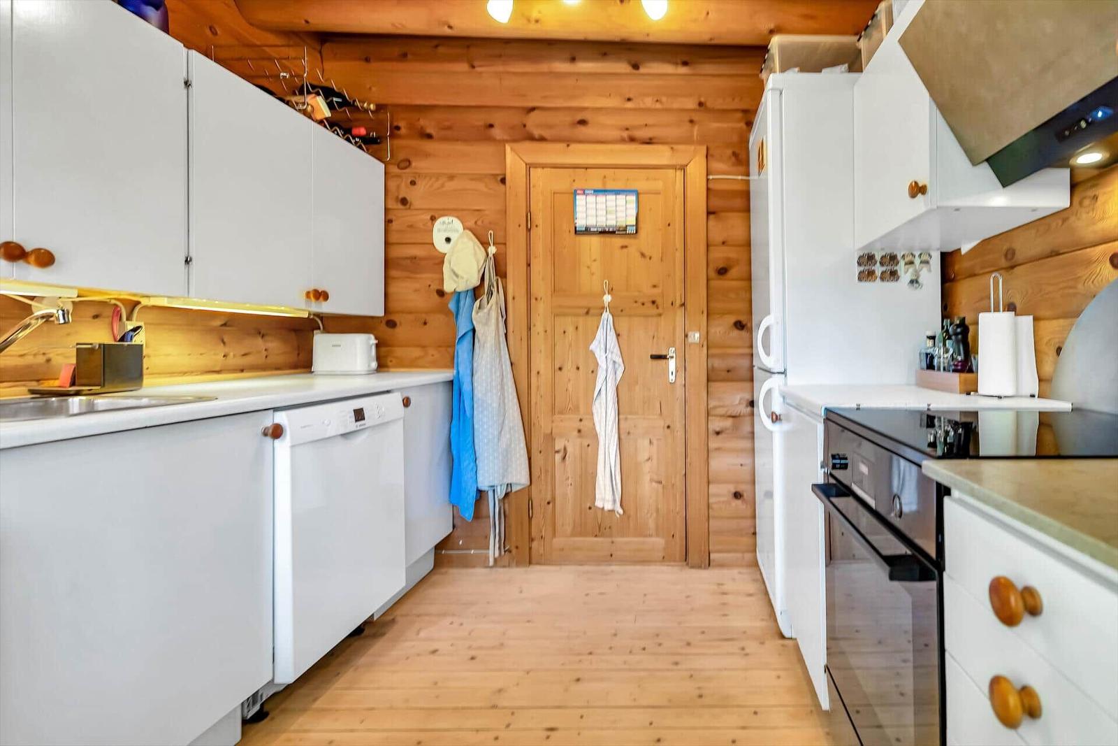 Küche mit weißen Schränken, Holzwand und Tür mit Haken.