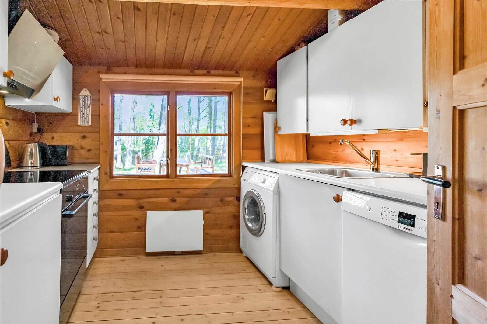Küche mit Waschmaschine und Spülmaschine, Holzwände und Fenster mit Blick auf den Garten.