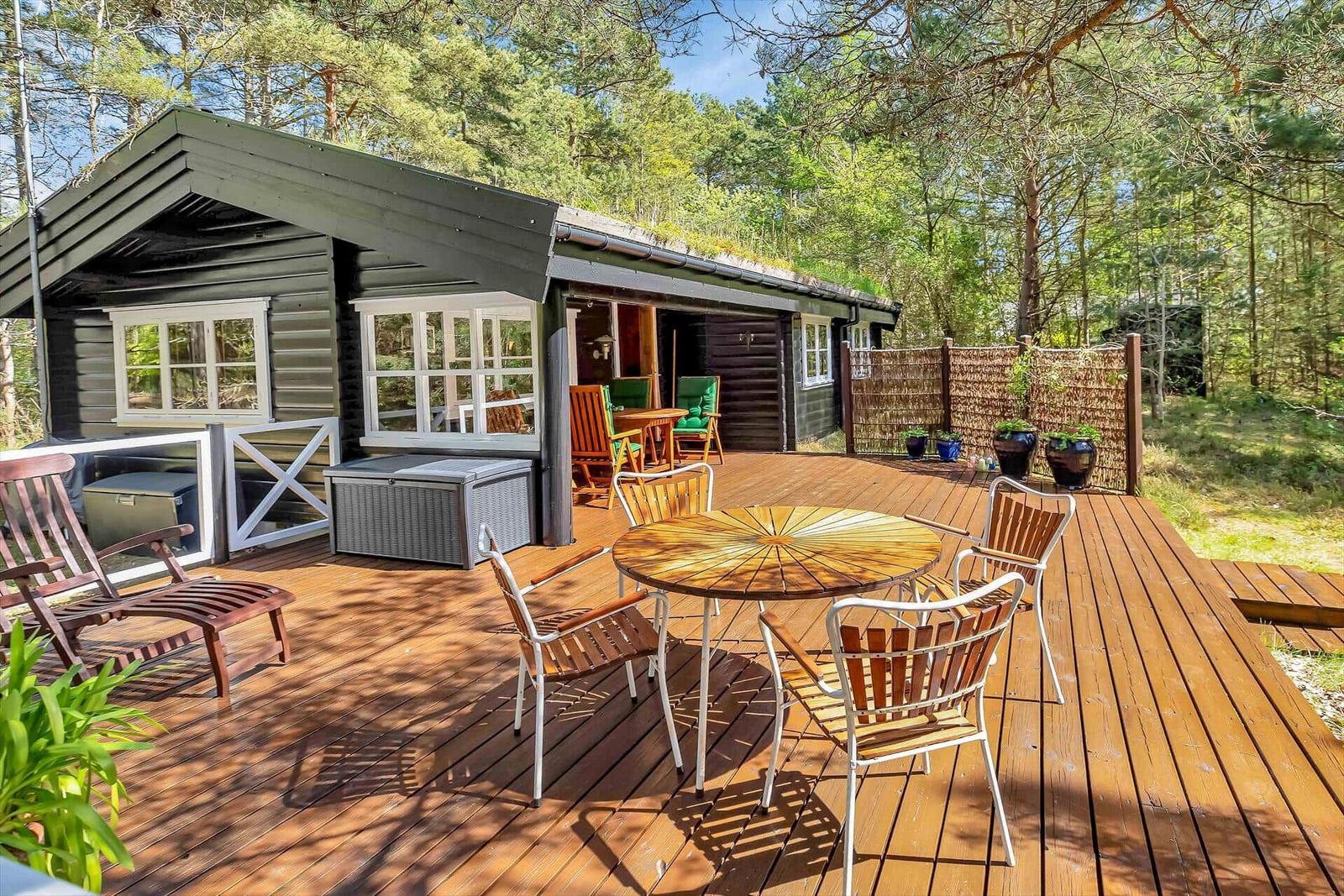 Holzterrasse mit Tisch und Stühlen vor einem Holzhaus im Wald