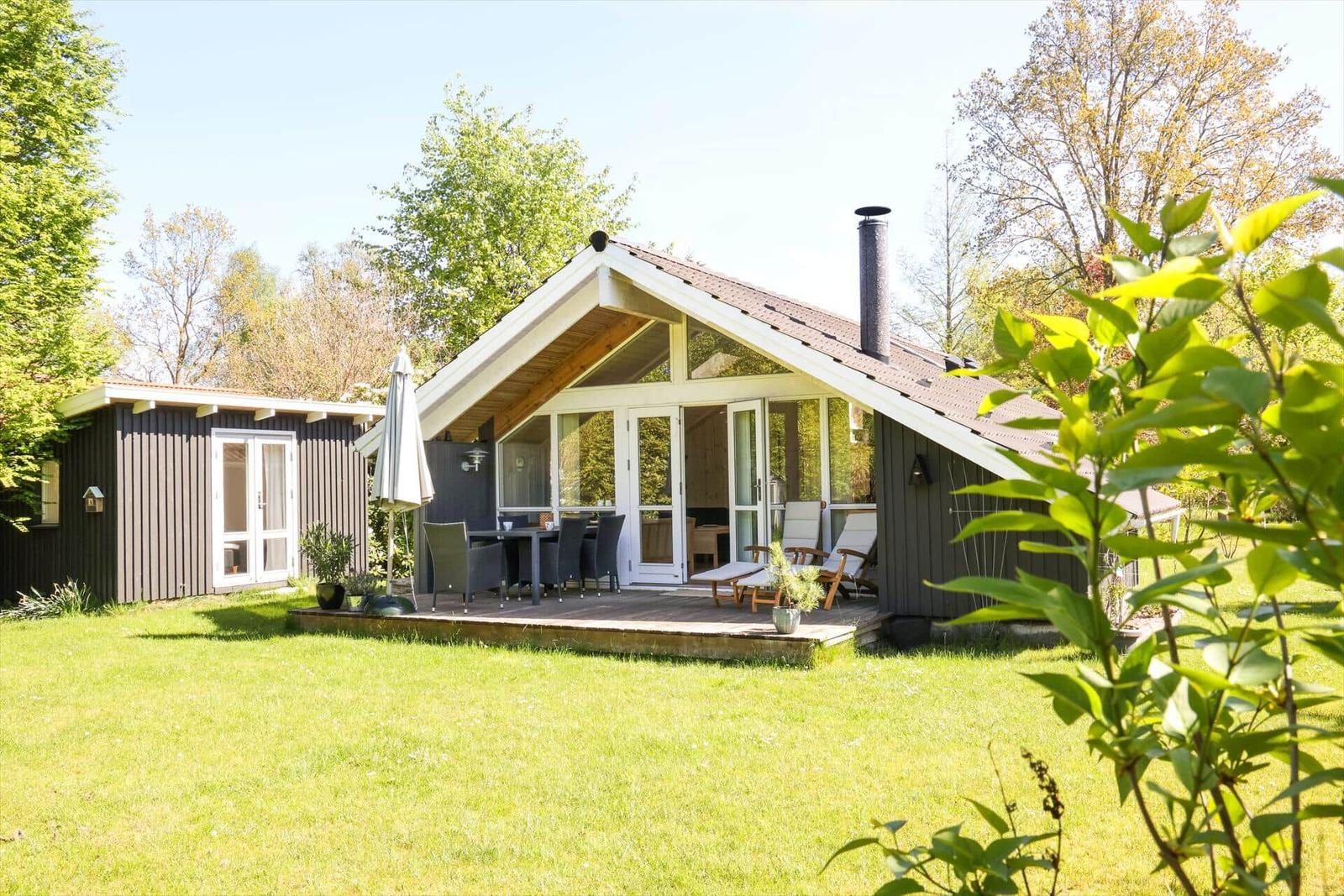 Haus mit Terrasse, Garten und Grillplatz. Holzhaus mit Schornstein und großen Fenstern.