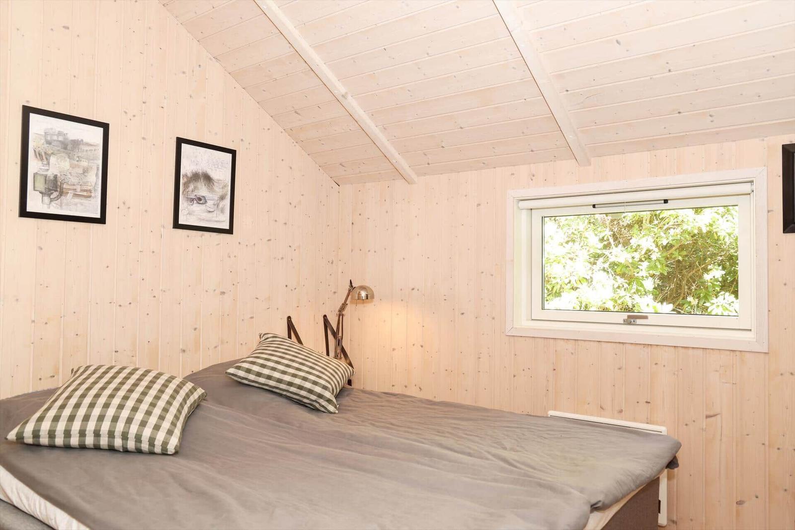 Schlafzimmer mit Holzwand, Bett und Fenster mit Blick auf Bäume.