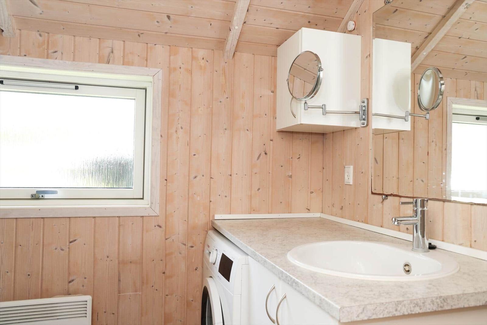 Badezimmer mit Waschmaschine, Waschtisch und Spiegelschrank an Holzwand