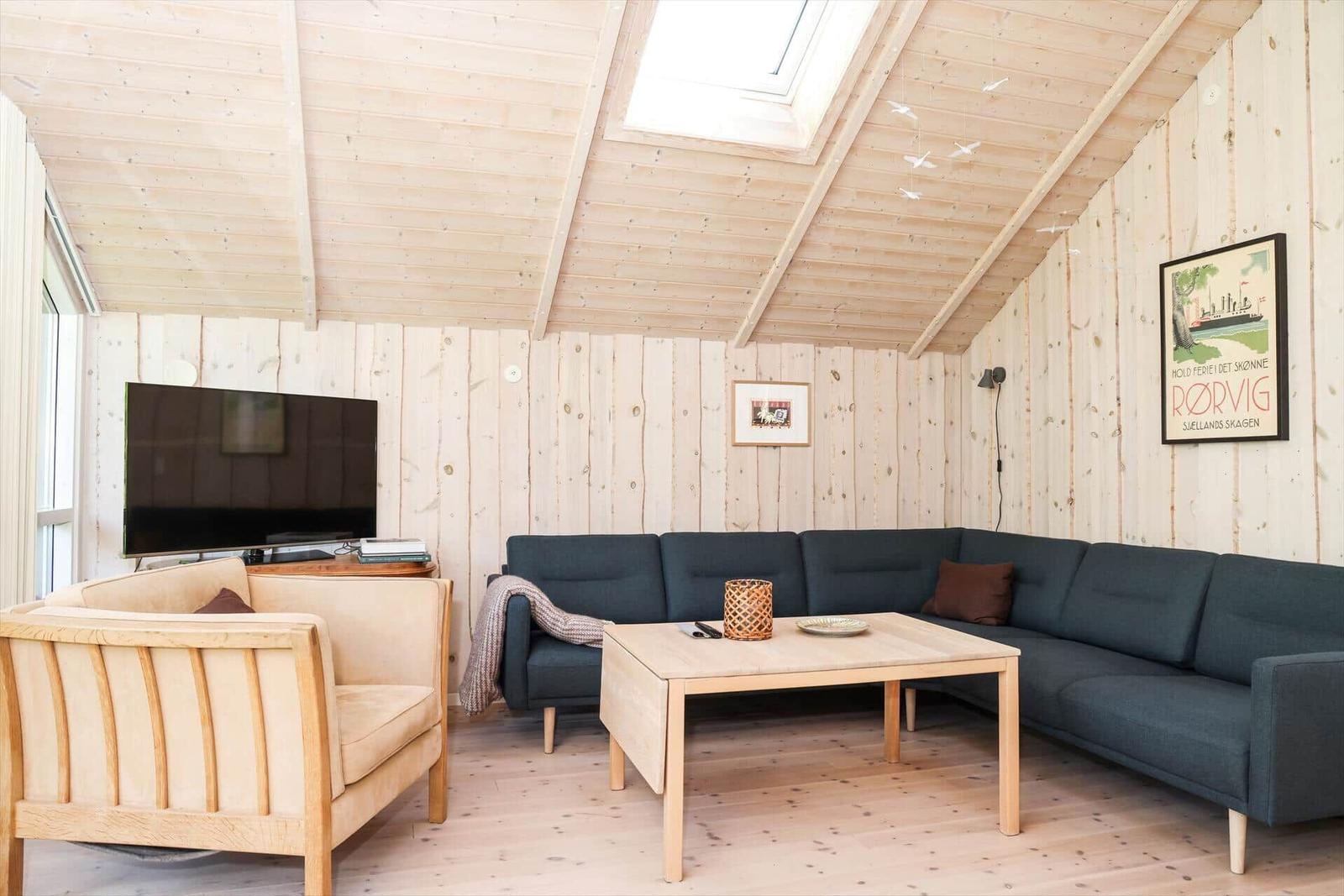 Wohnzimmer mit Holzwand, Sofa, Sessel und Fernseher unter Dachschräge.