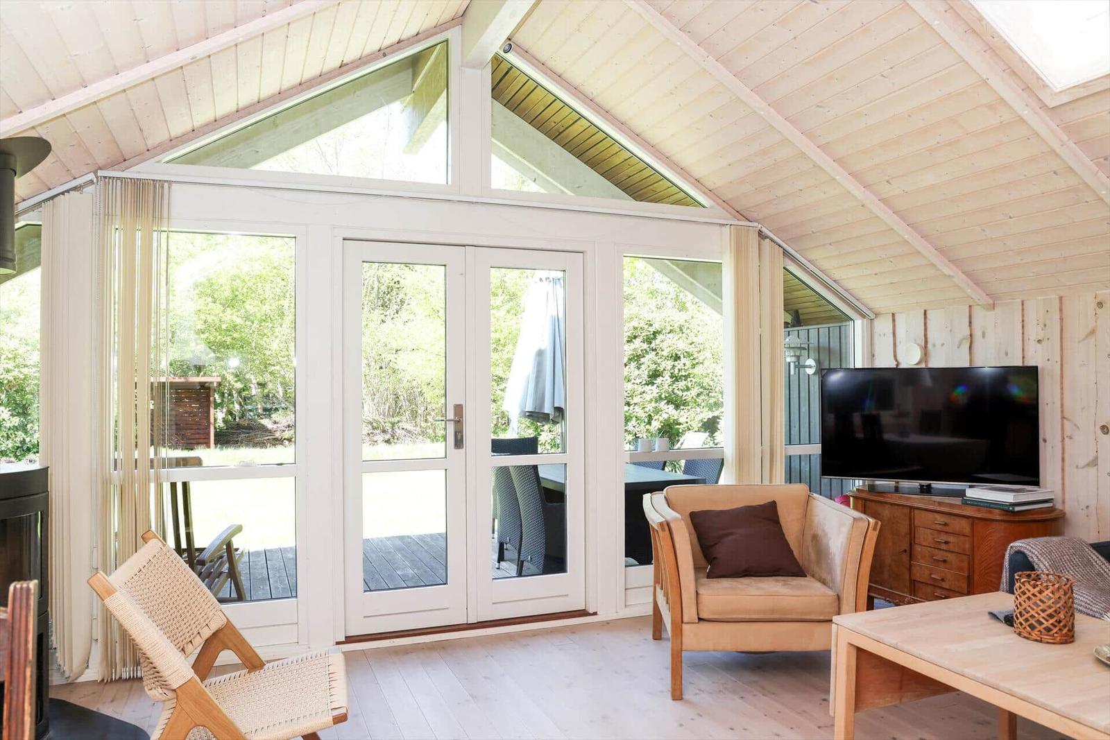 Wohnbereich mit Sitzgelegenheiten, Fernseher und großem Fenster zum Garten.