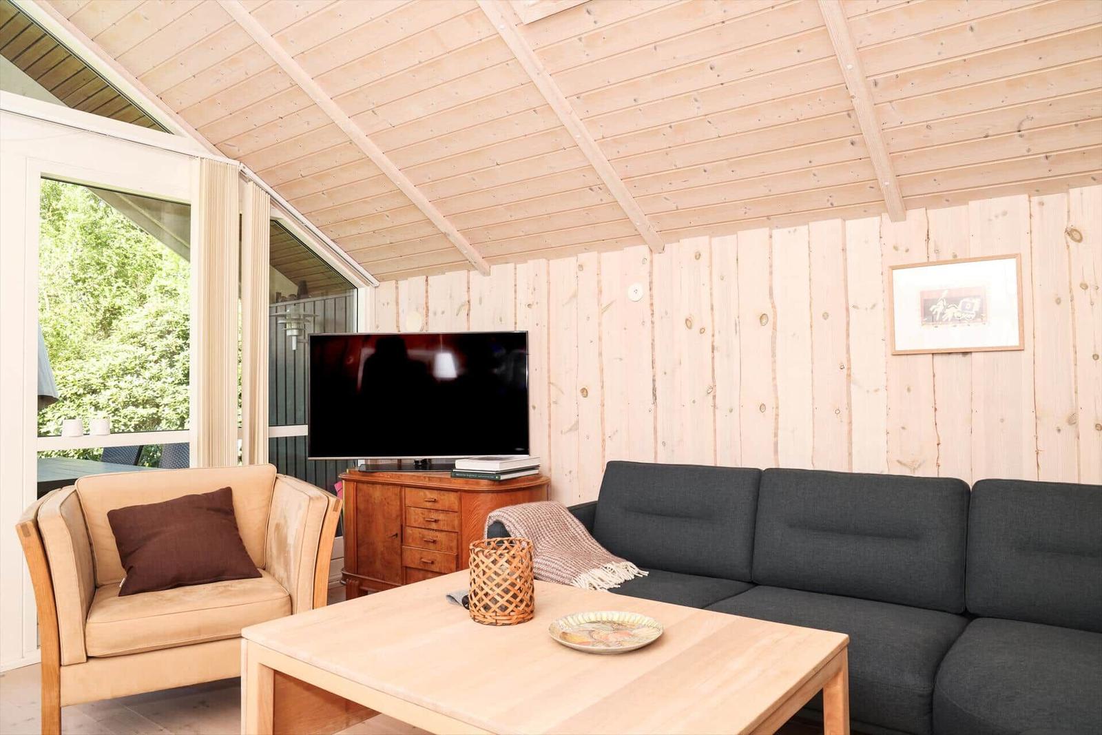 Wohnzimmer mit Sofa, Sessel, Couchtisch und Fernseher an Holzwand.