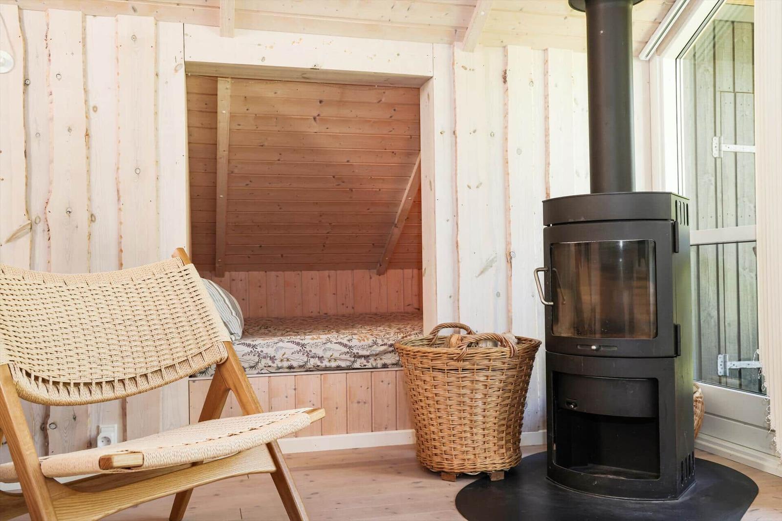 Raum mit Holzwand, Bett, Stuhl und Kaminofen.