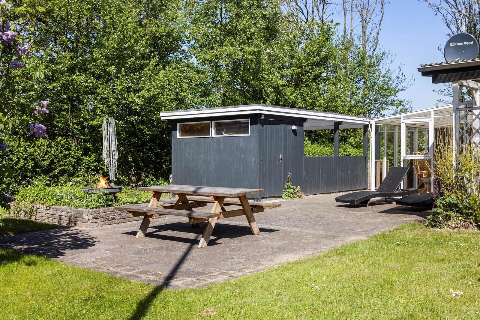 Garden with picnic table, loungers, and fire pit beside gray wooden house.