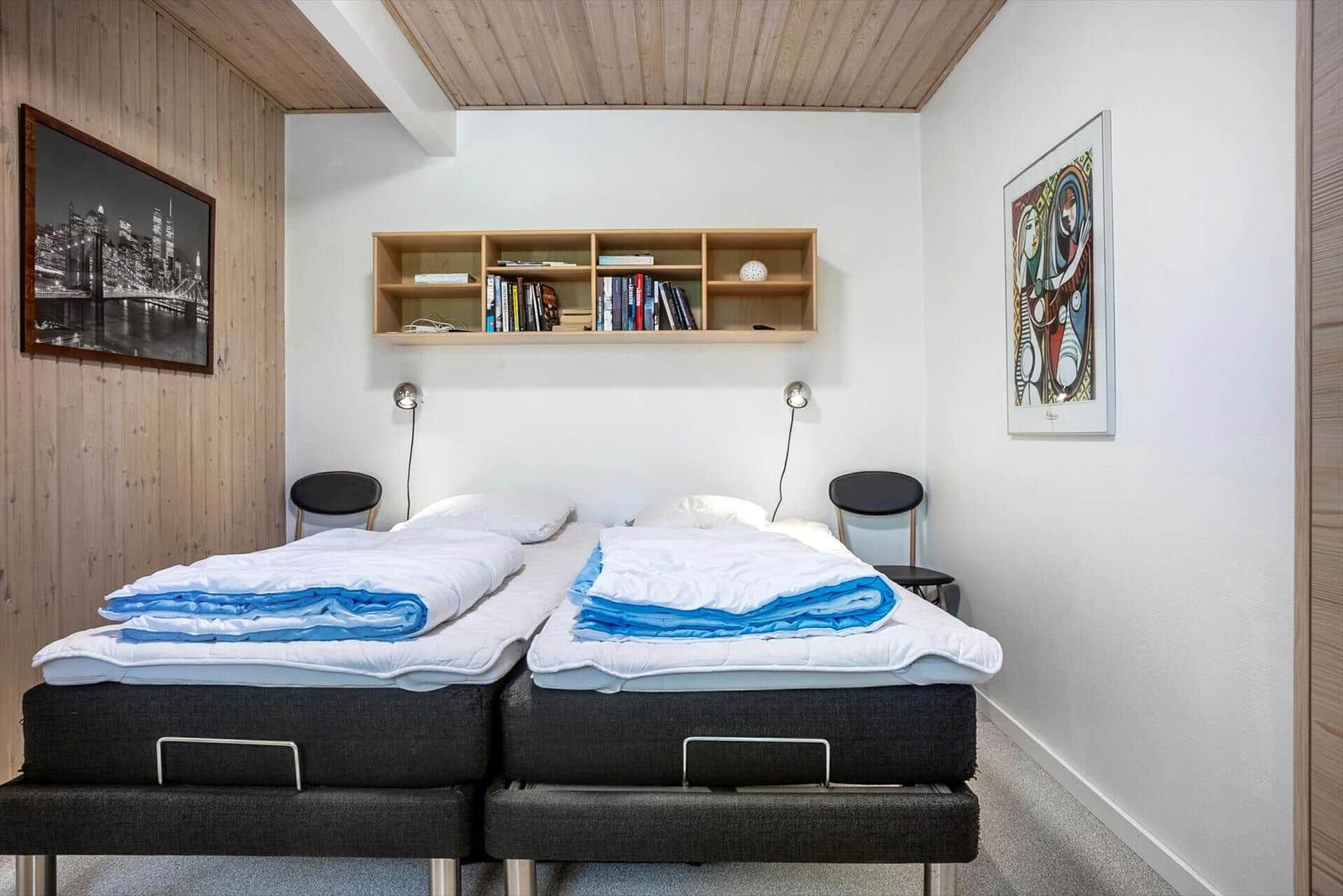 Two beds with blue blankets, bookshelf, and wall art.