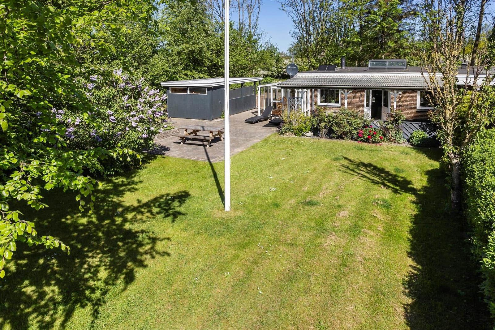 House with garden, terrace, and barbecue area. Surrounded by trees and flowers.