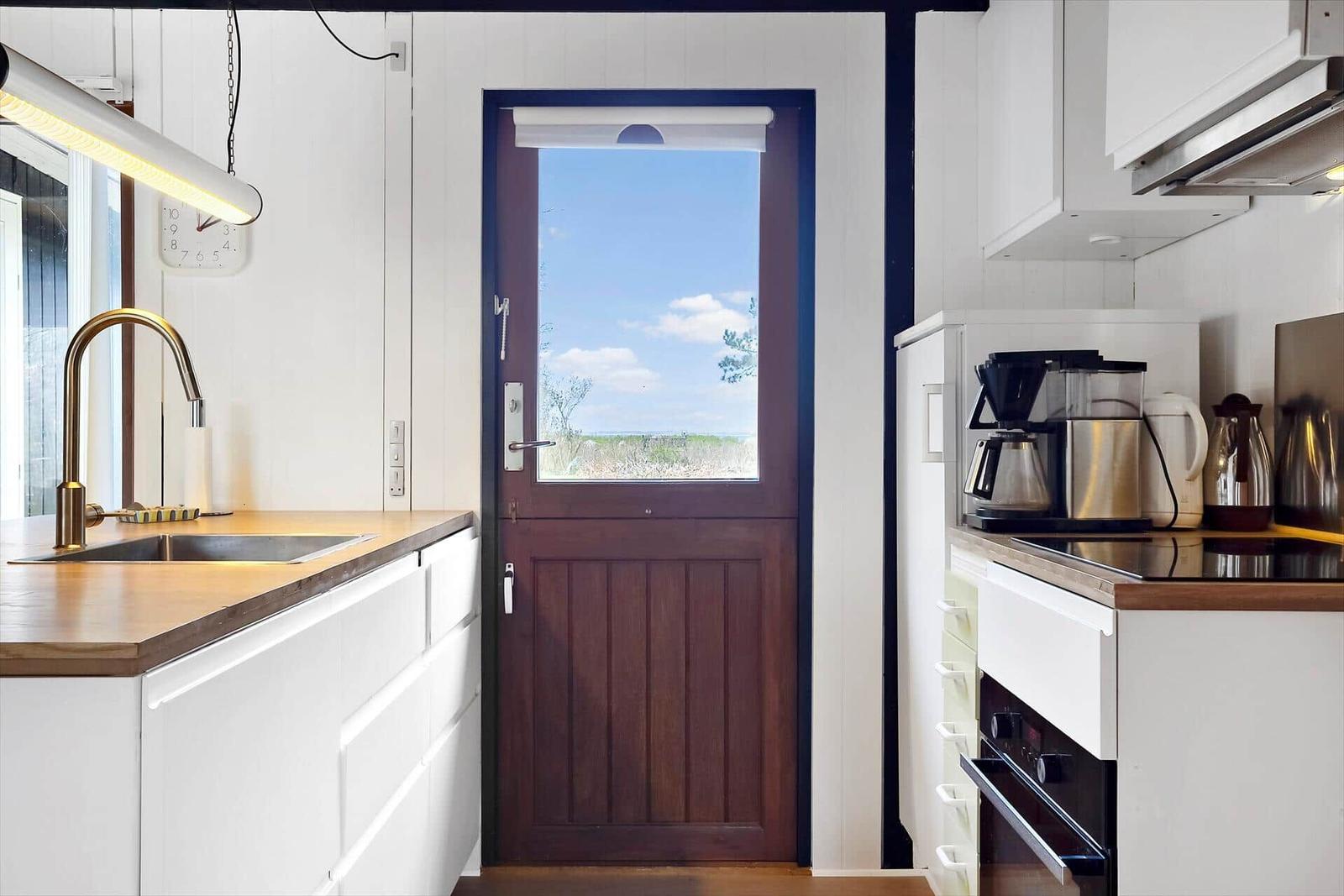Küche mit Holz Arbeitsplatte, Tür mit Blick auf Landschaft, Edelstahl Geräte und goldener Wasserhahn.