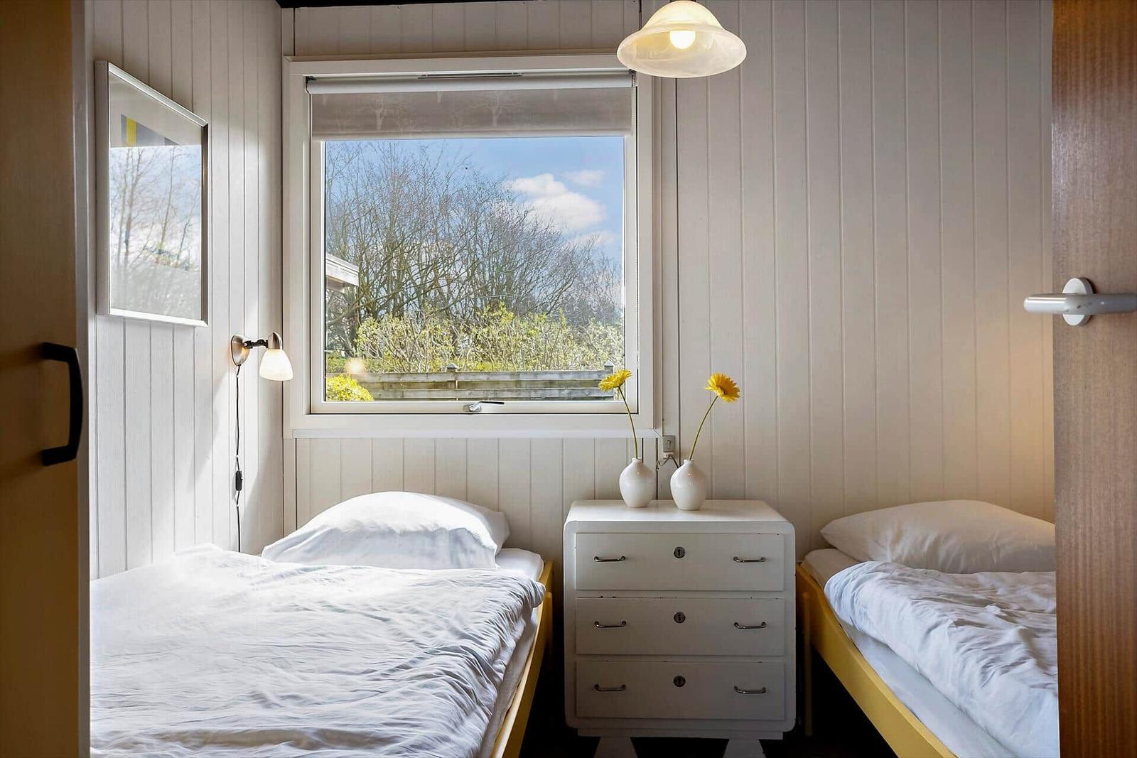 Zwei Betten mit weißer Bettwäsche stehen an einem Fenster mit Blick auf Bäume.