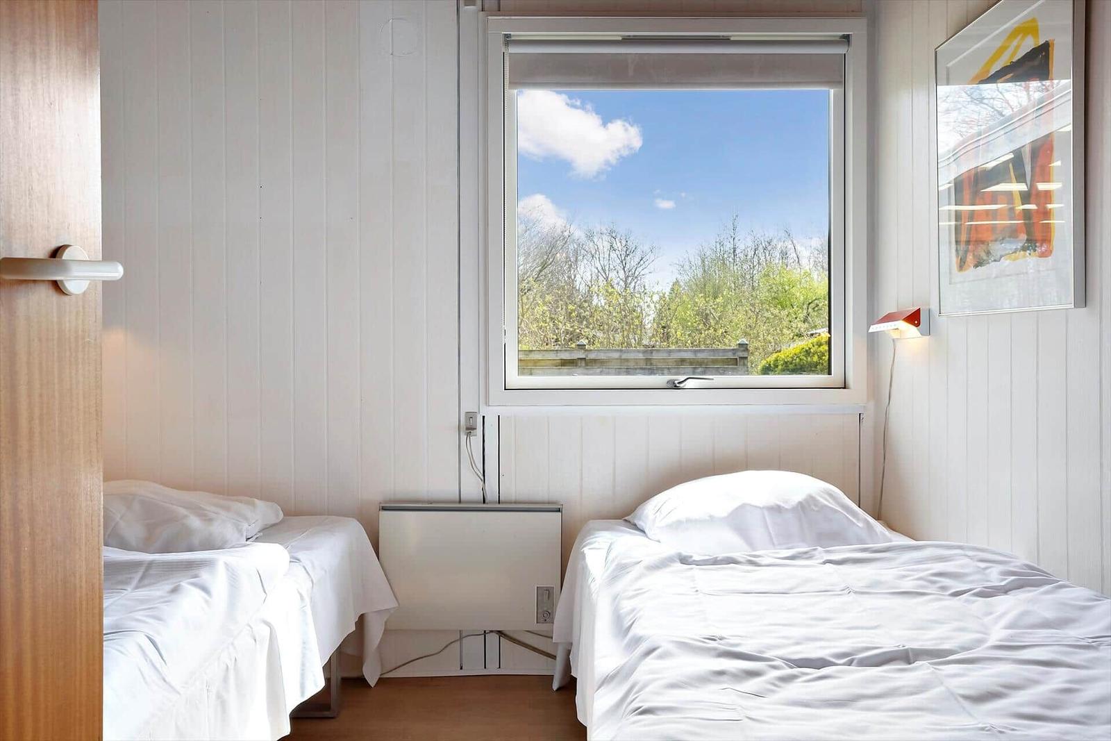 Zwei Betten mit weißen Bettwäsche, Fenster mit Blick auf Bäume und Himmel.