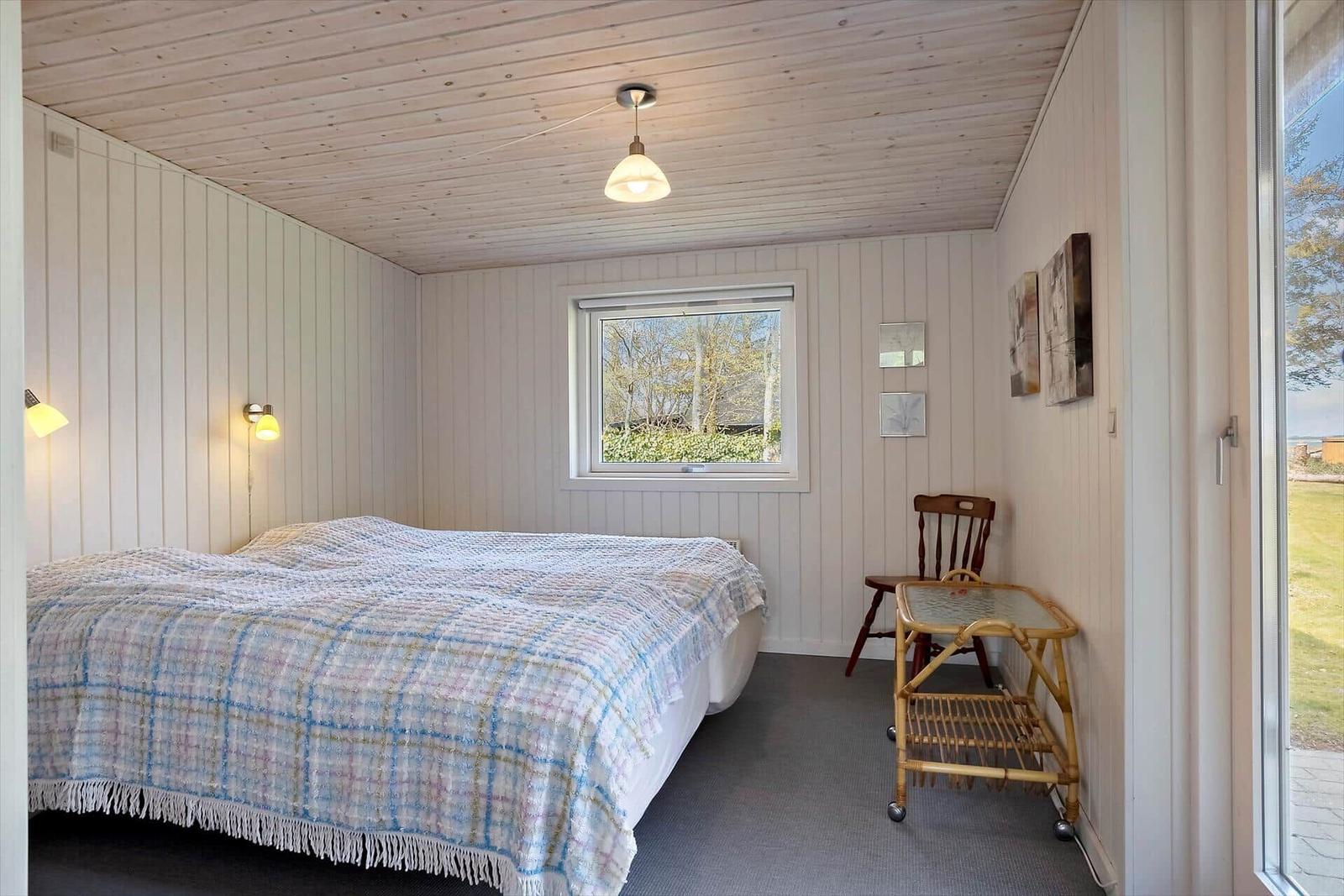 Schlafzimmer mit Bett, Fenster, Stuhl und Wandschrank. Holzwand und Decke.