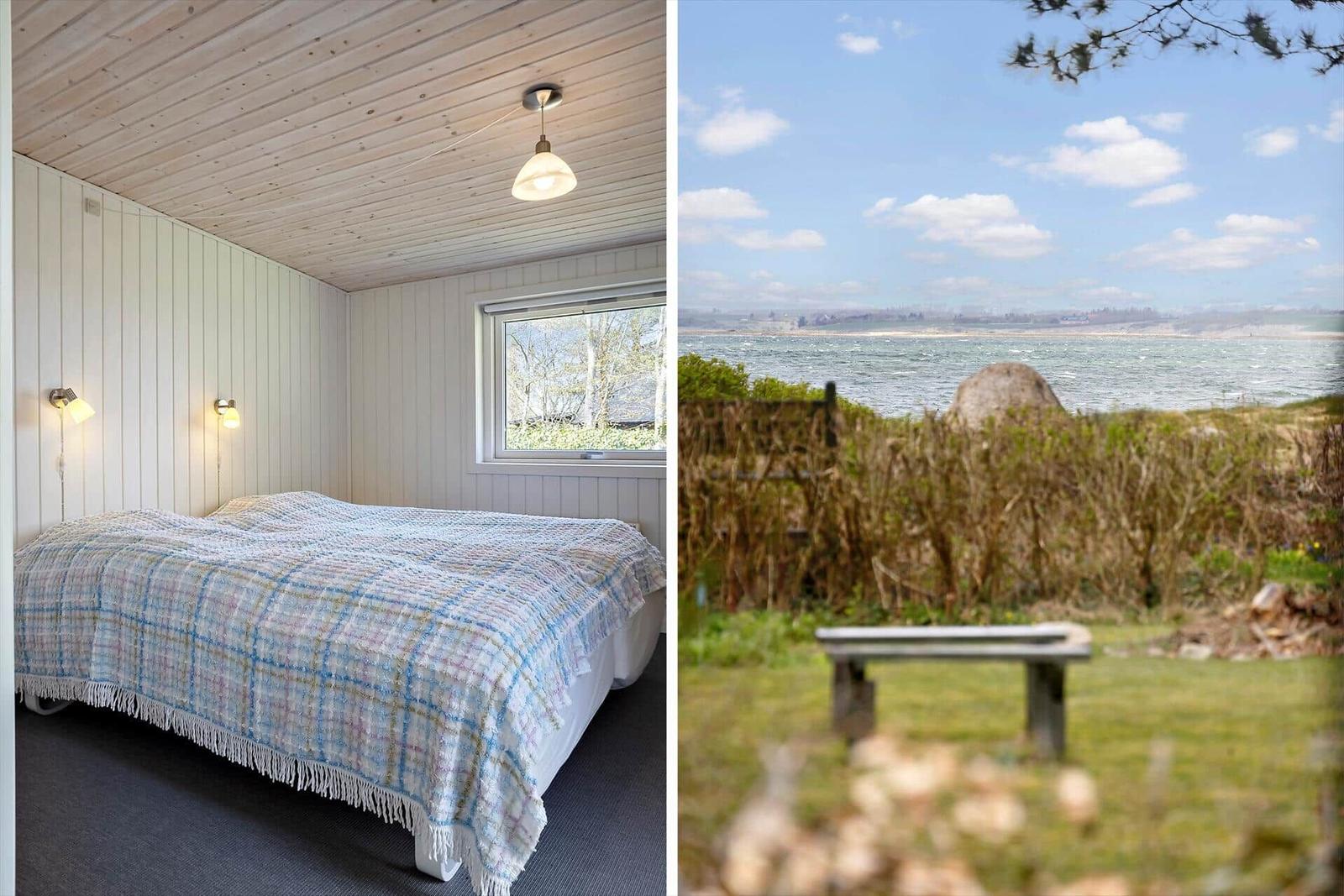 Schlafzimmer mit Bett und Fenster. Außen: Blick auf Wasser mit Bank.