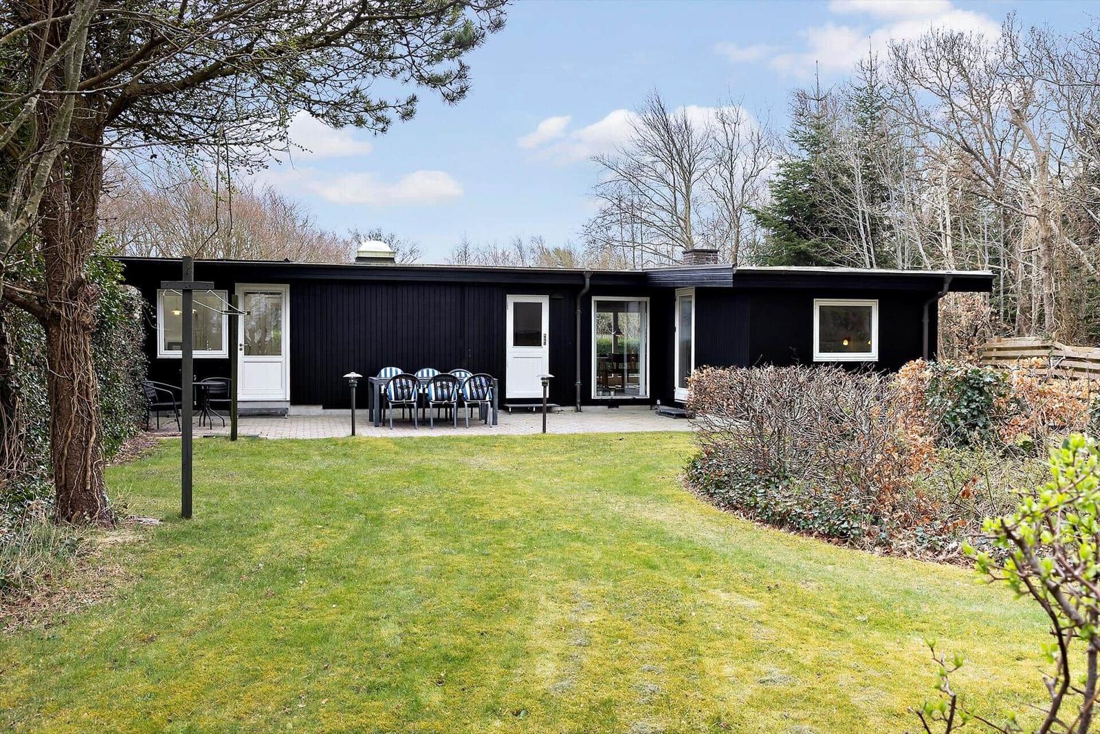 Schwarzes Haus mit Terrasse, Garten und Bäumen im Hintergrund.