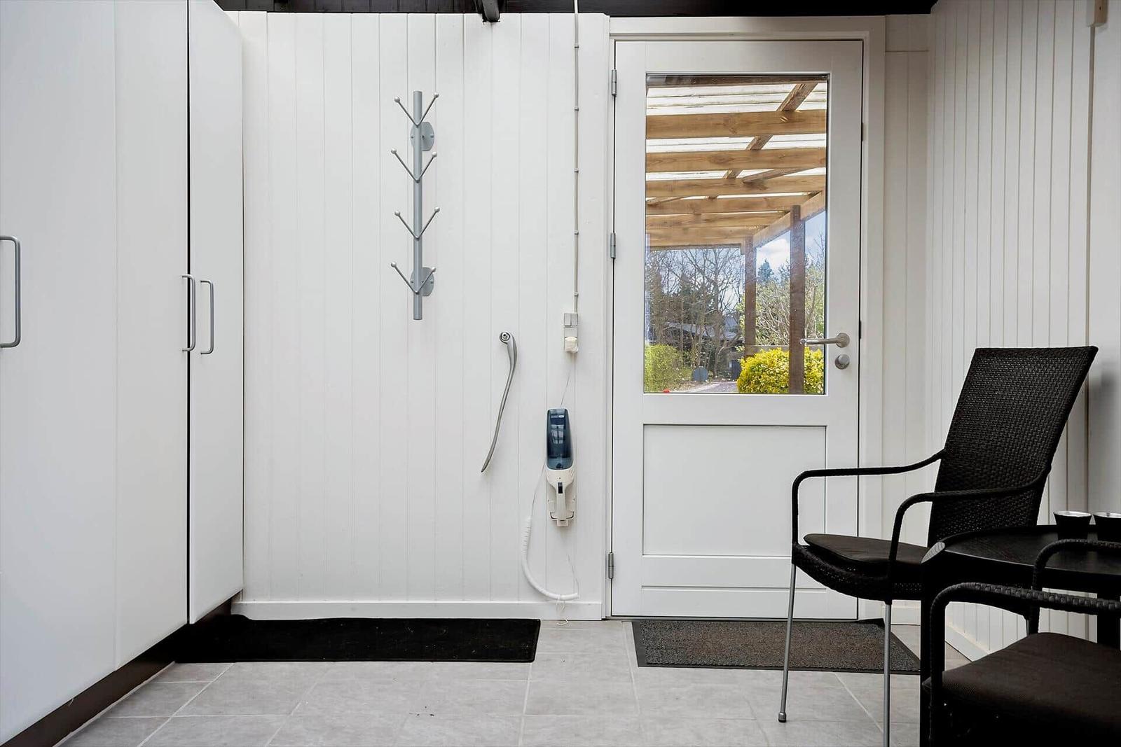 Helle Eingangshalle mit weißen Wänden, Tür und Garderobe. Außenterrasse mit Sitzgelegenheit sichtbar.