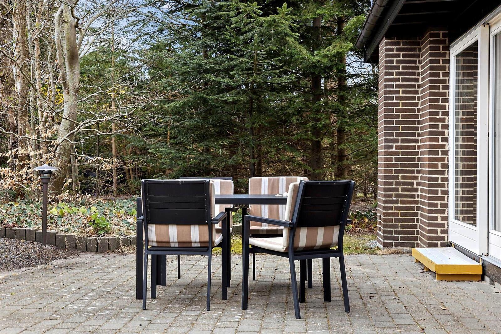 Terrasse mit Tisch und Stühlen neben Haus mit Backsteinwand.