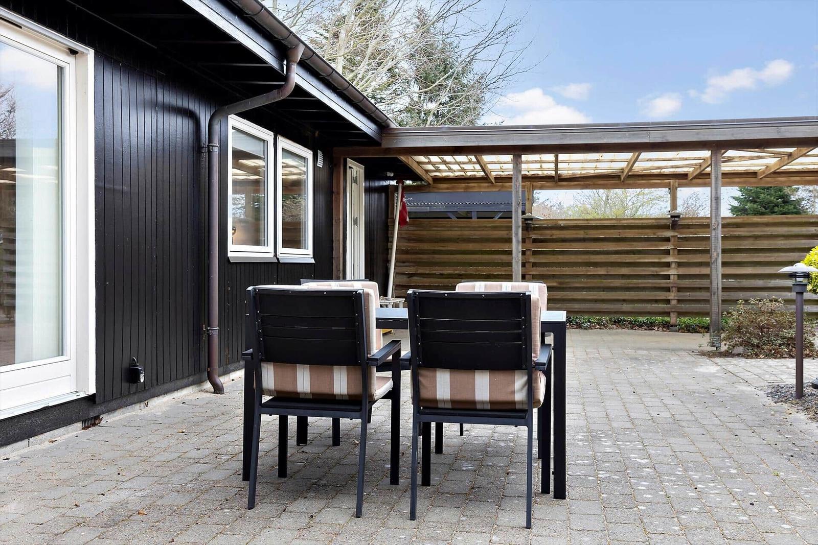 Terrasse mit Tisch und Stühlen vor schwarzem Haus mit Holzüberdachung.