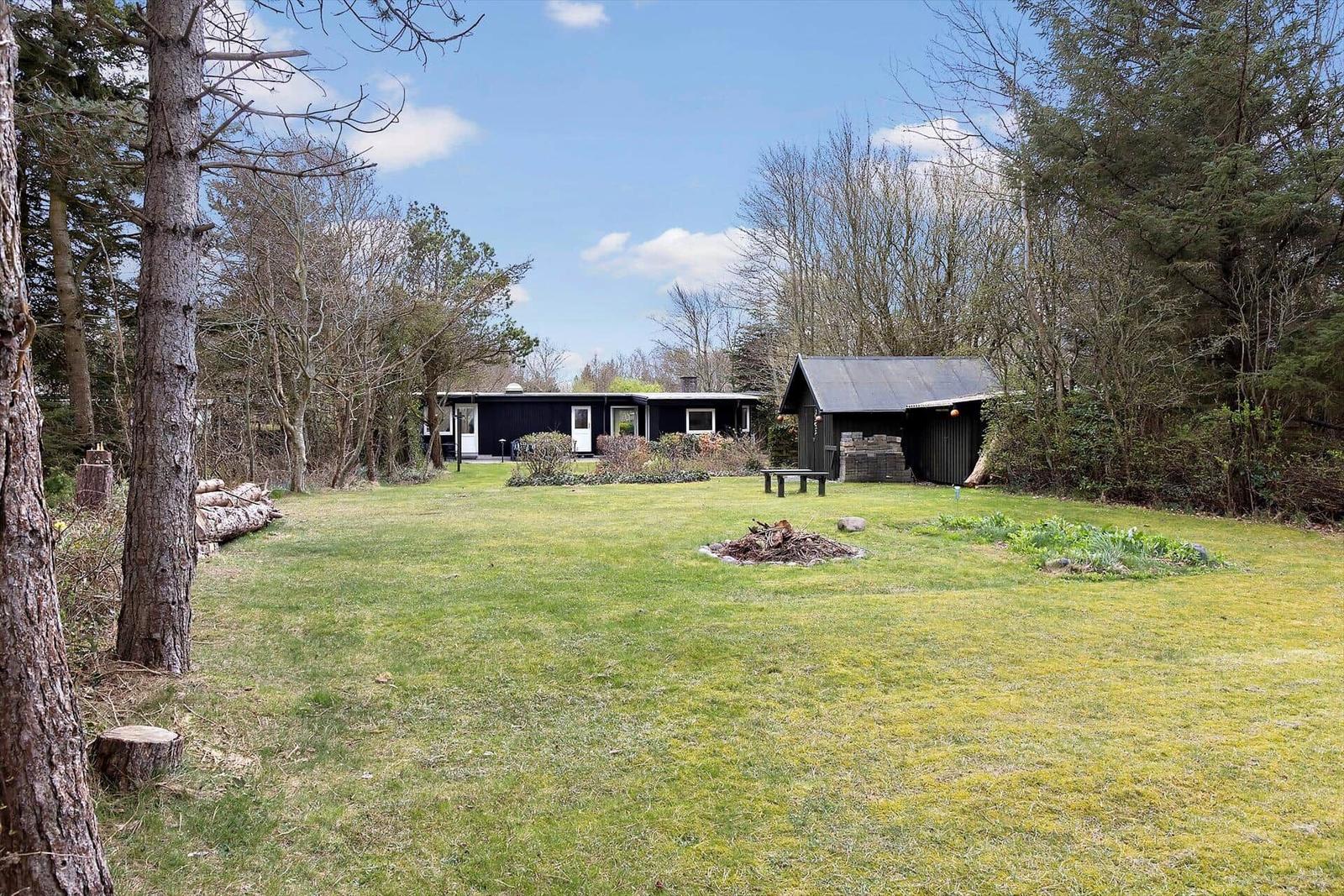 Schwarzes Haus mit Garten, Holzstapel und kleiner Hütte im Wald.