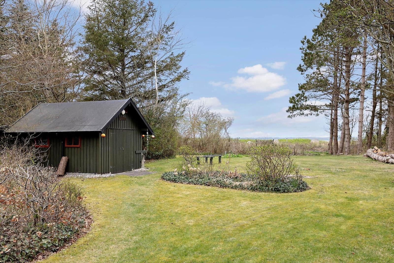 Ein grünes Holzhaus mit Garten, Tisch und Bäumen im Hintergrund.