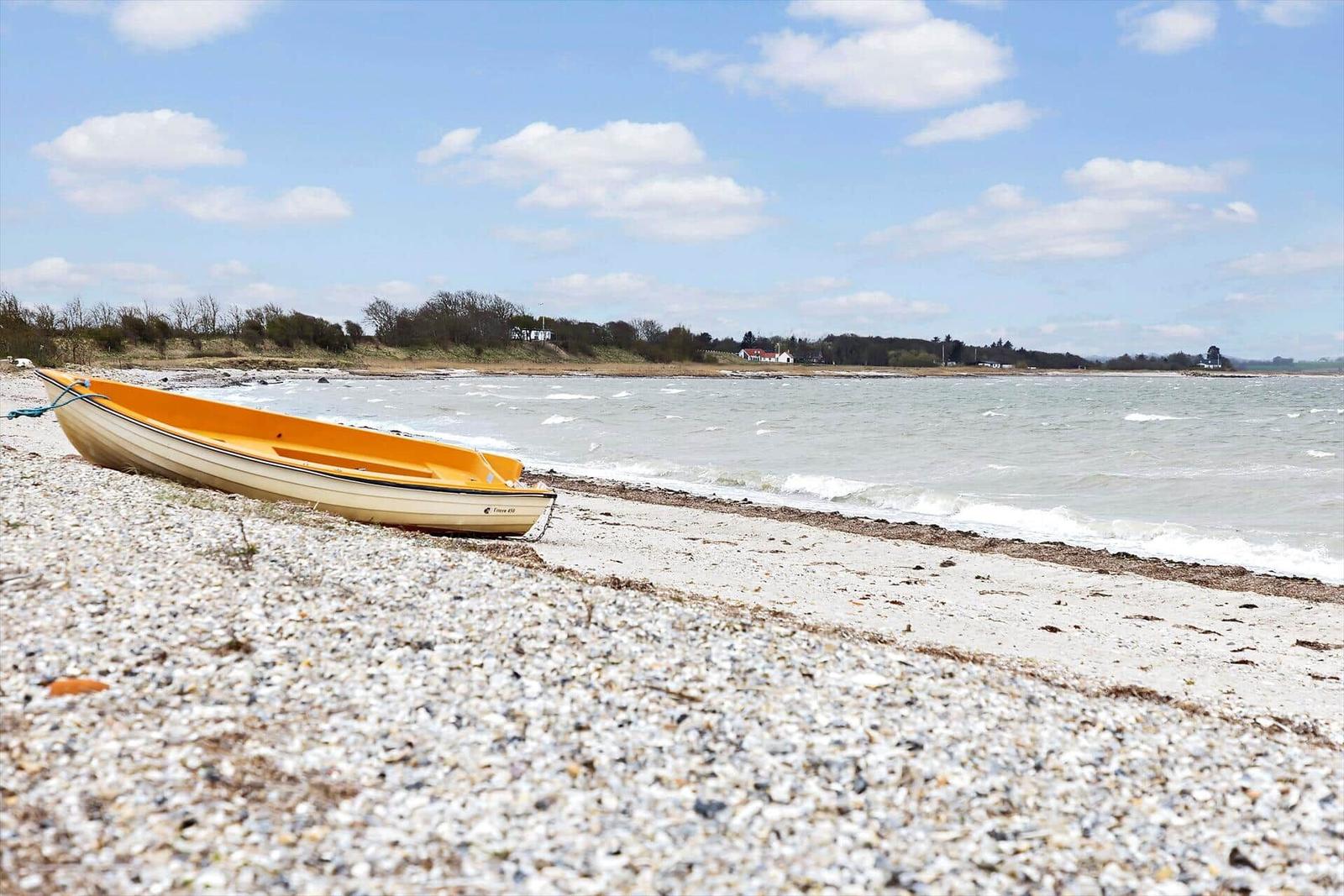 Ein gelbes Boot liegt am steinigen Strand. Im Hintergrund erstreckt sich das Wasser unter einem blauen Himmel.